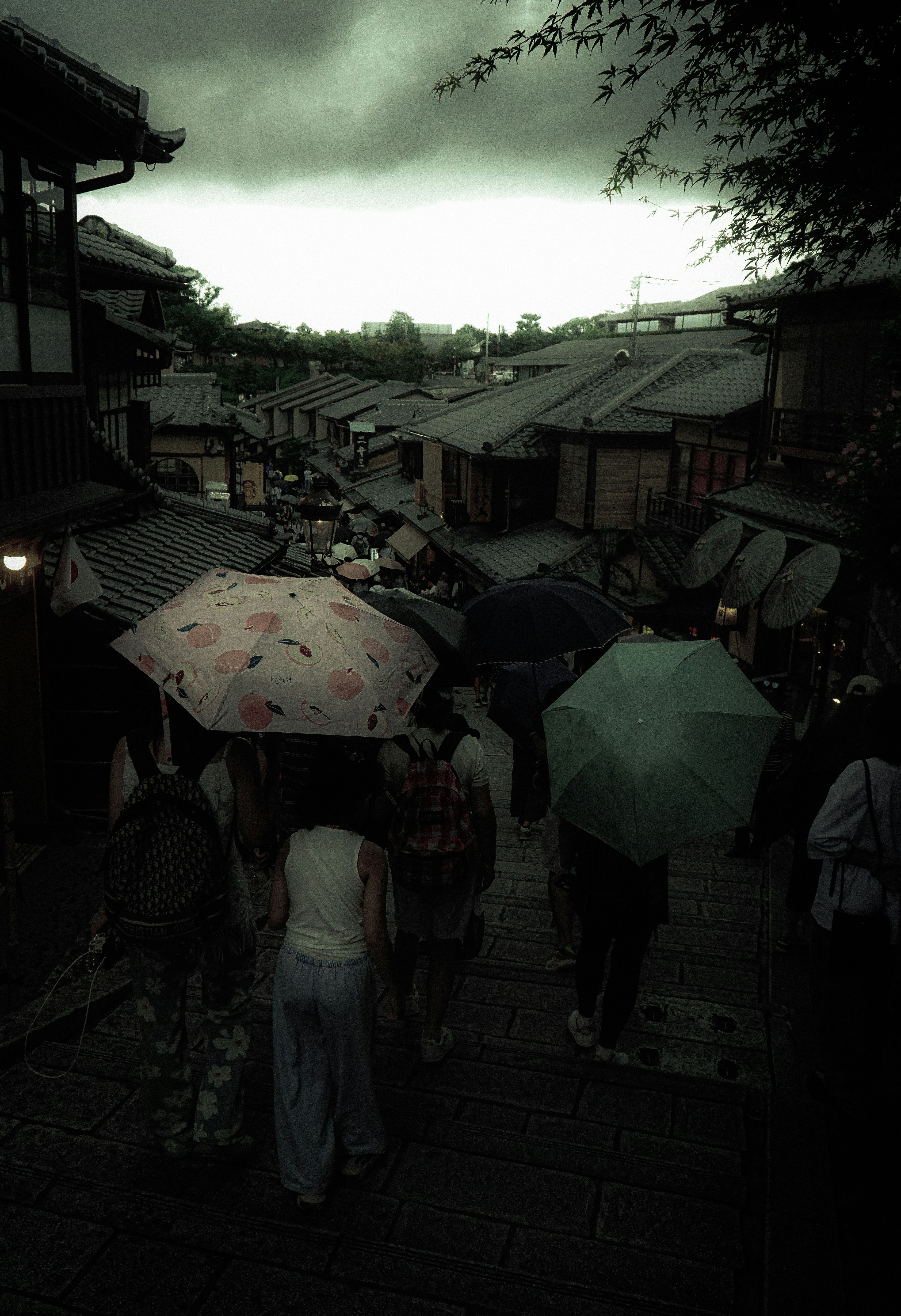 雨の中を歩く人々が傘をさし、古い町並みが背景にある風景