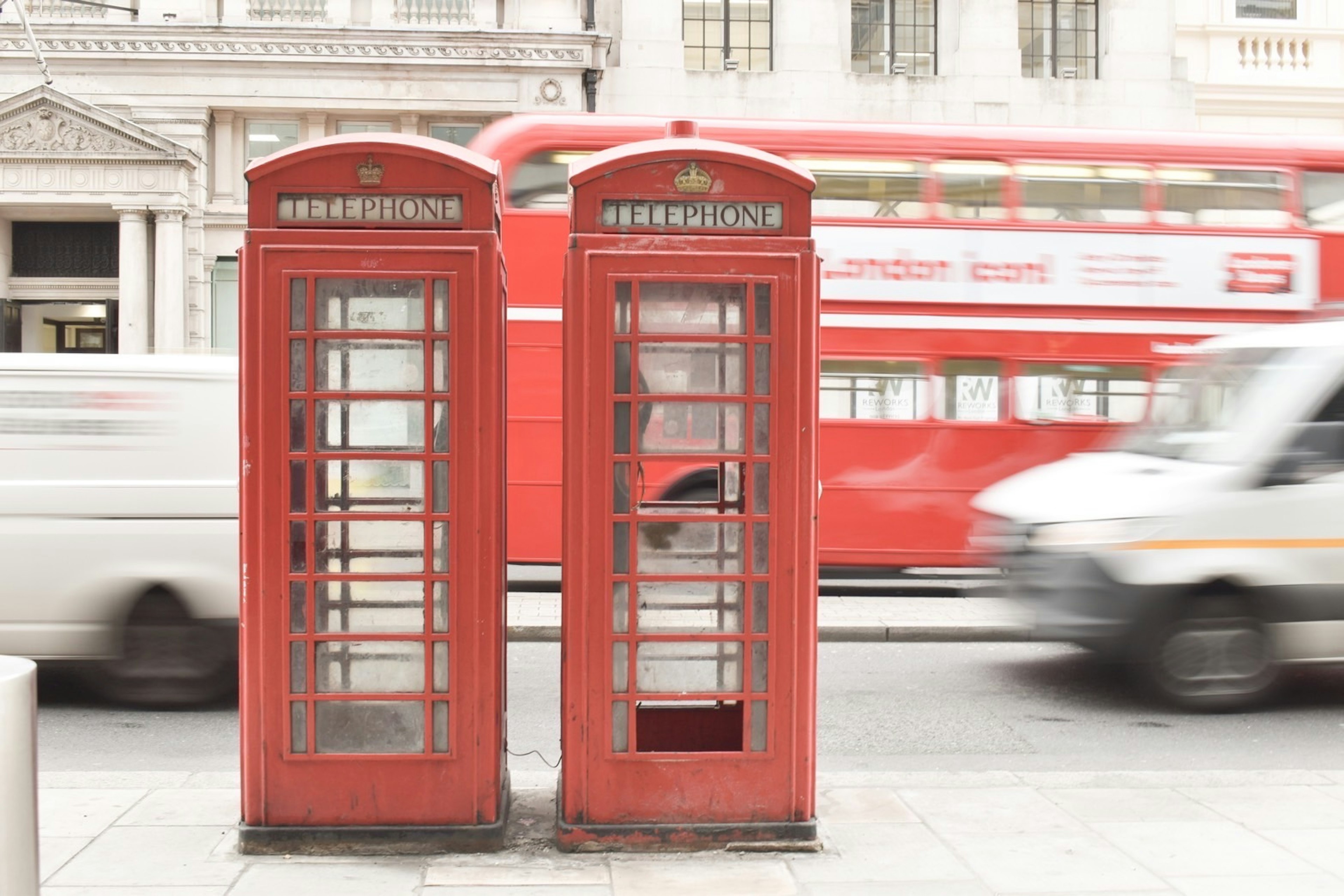 Two iconic red telephone booths in London with a bus in the background