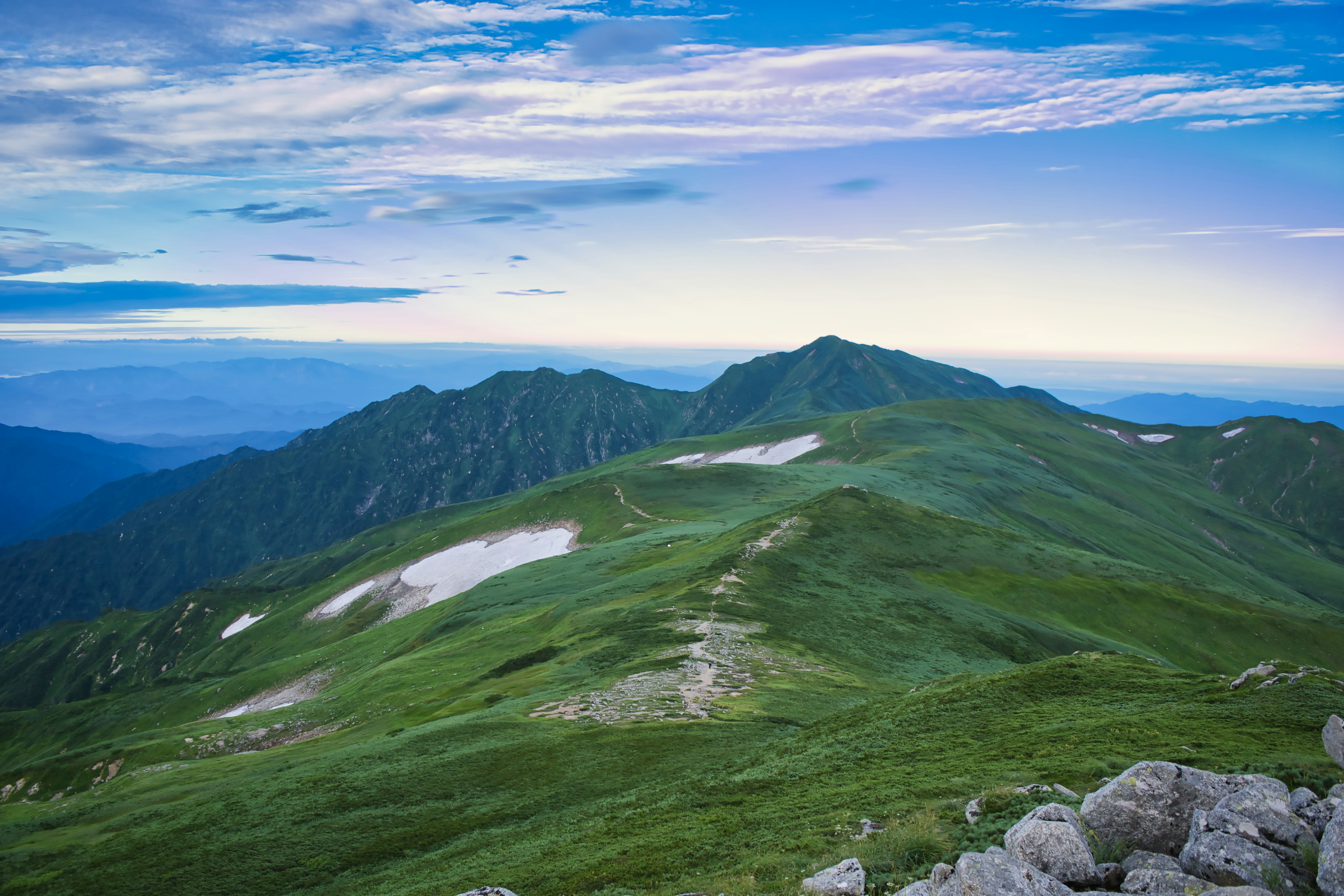 Vista escénica de montañas verdes bajo un cielo azul con algunas manchas de nieve