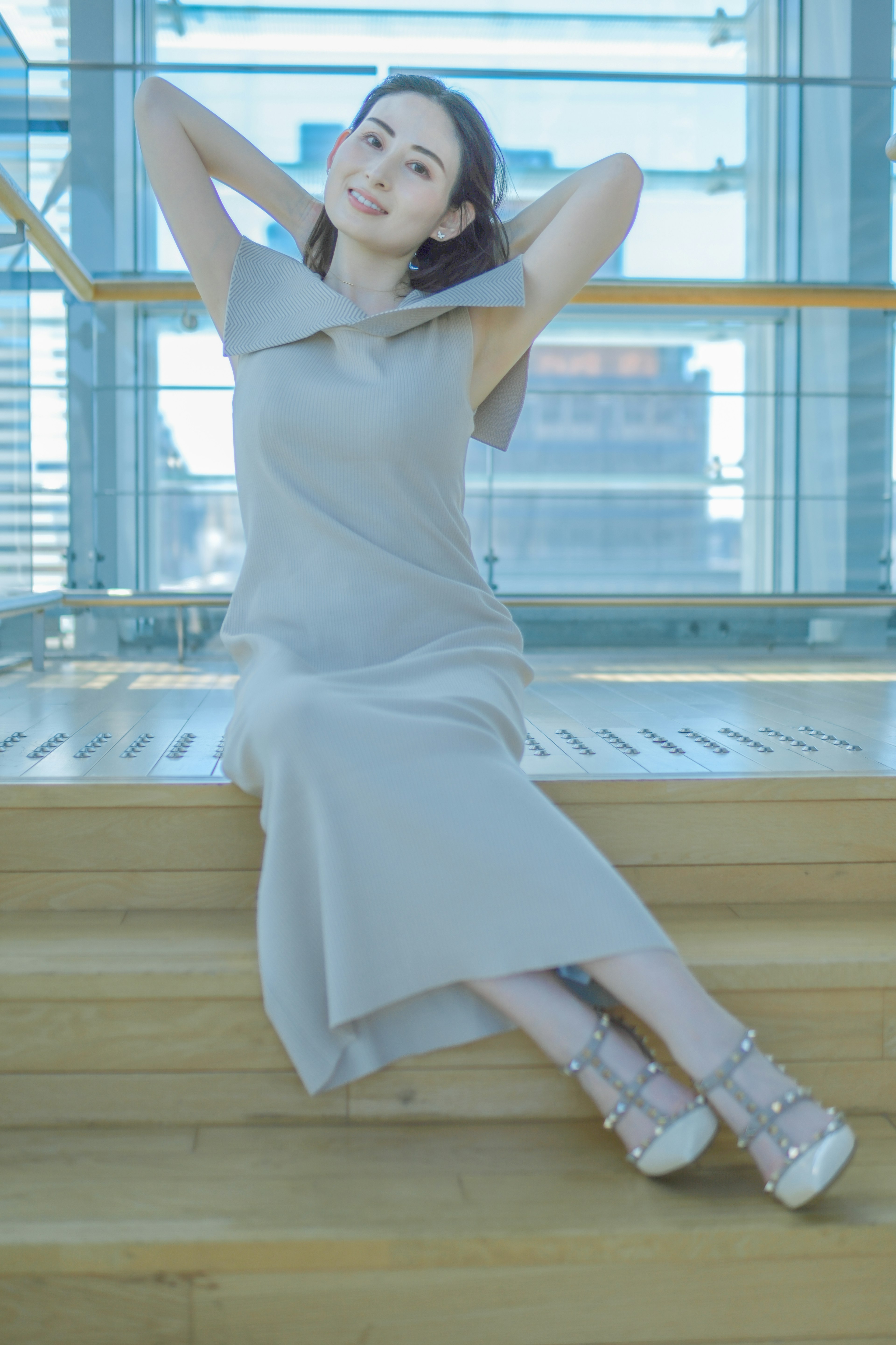 A woman sitting by a bright window wearing a simple gray dress