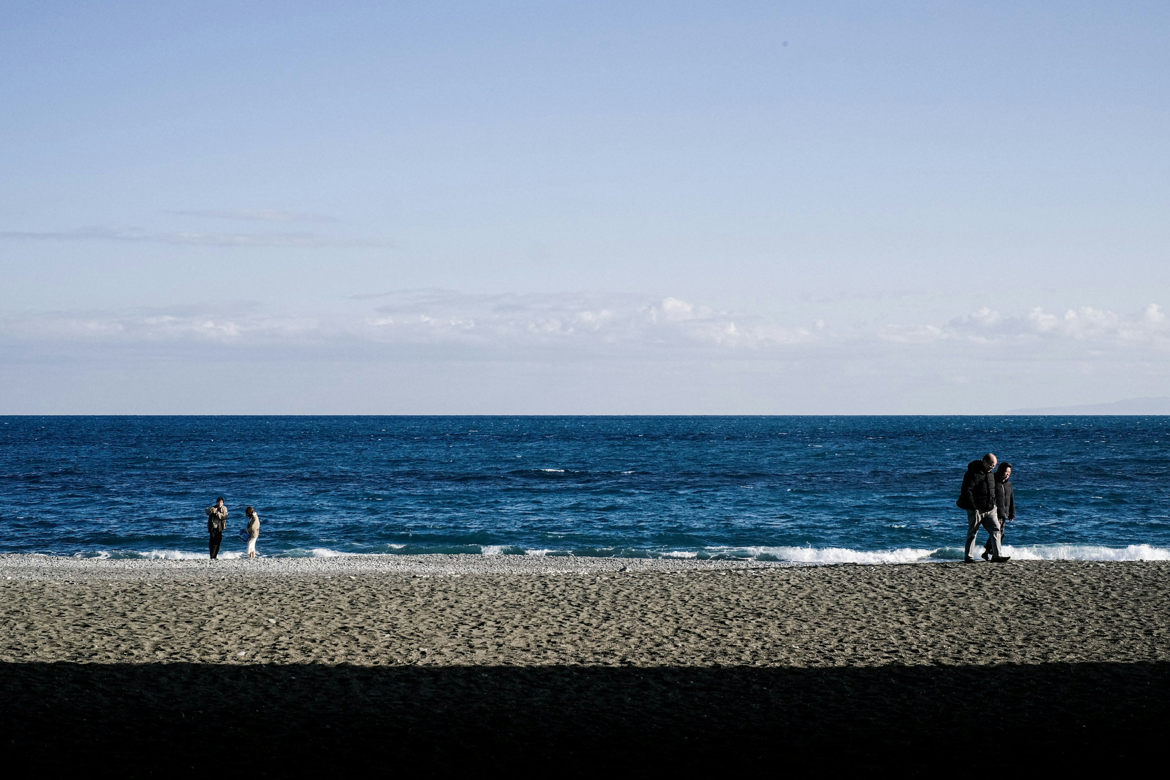 青い海と空が広がるビーチで人々が散歩している風景