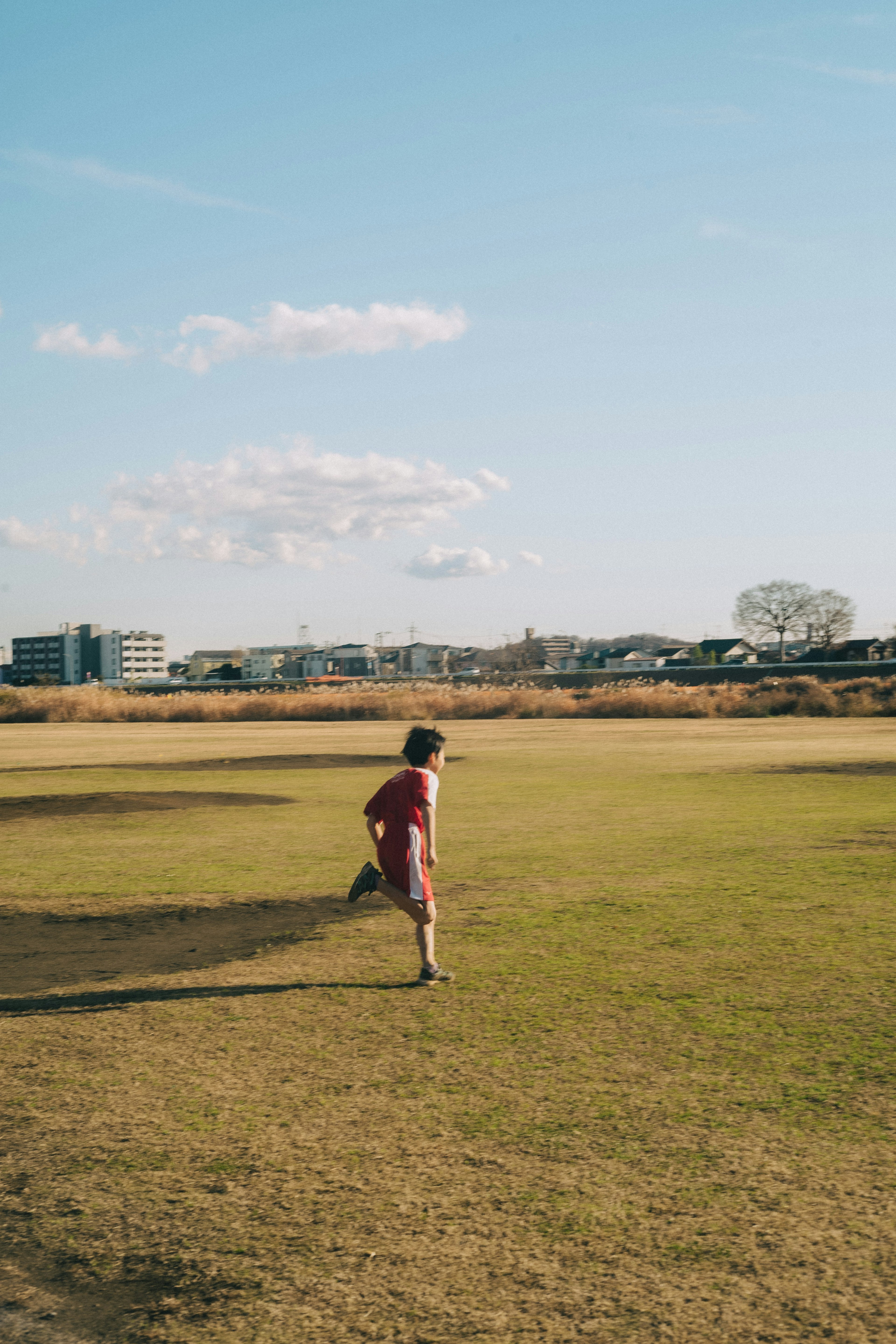 Un niño corriendo sobre la hierba bajo un cielo azul con edificios al fondo