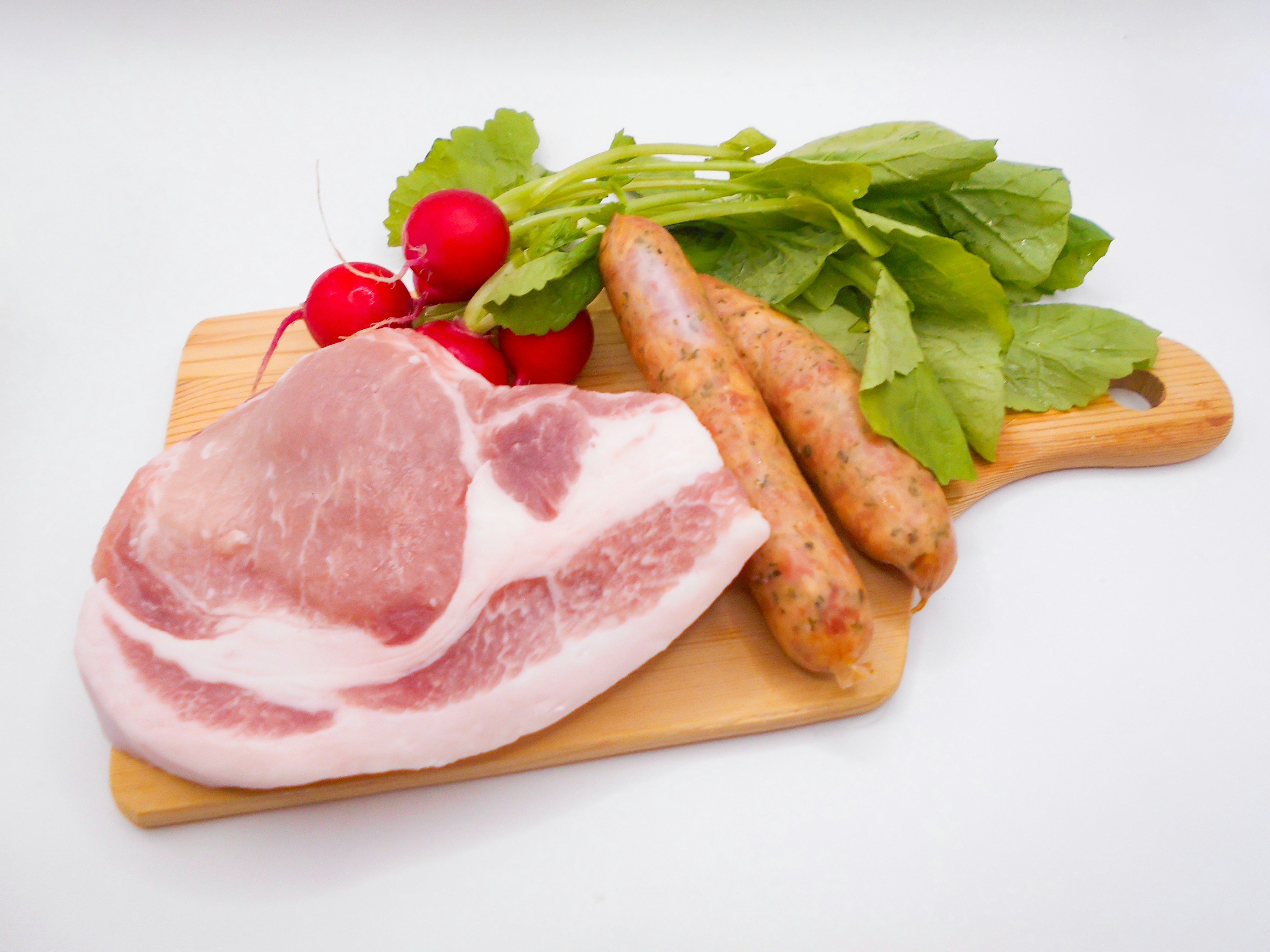 Raw slices of pork and sausages with radishes and leafy greens on a wooden cutting board