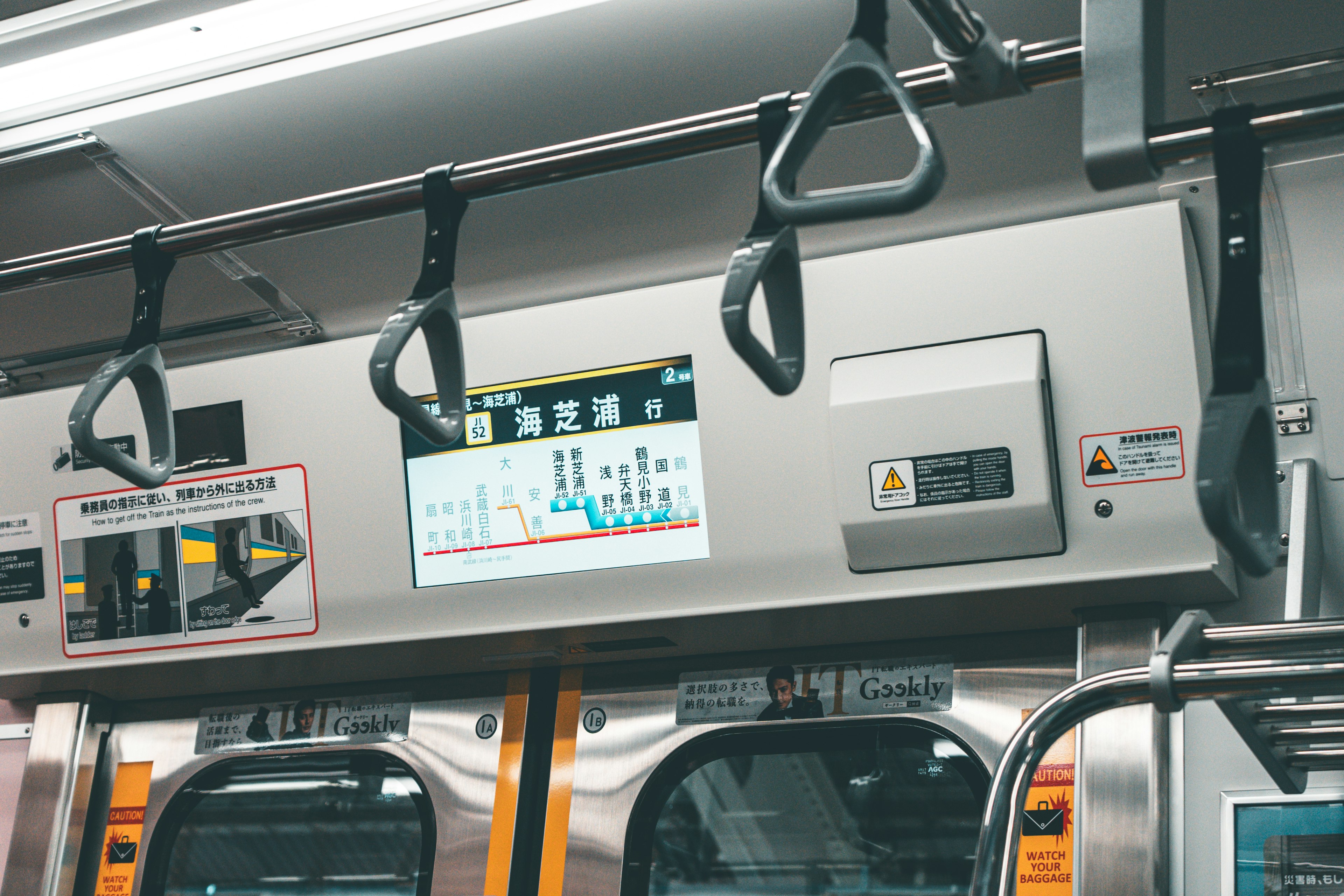 Interno di un treno con maniglie sospese e uno schermo informativo