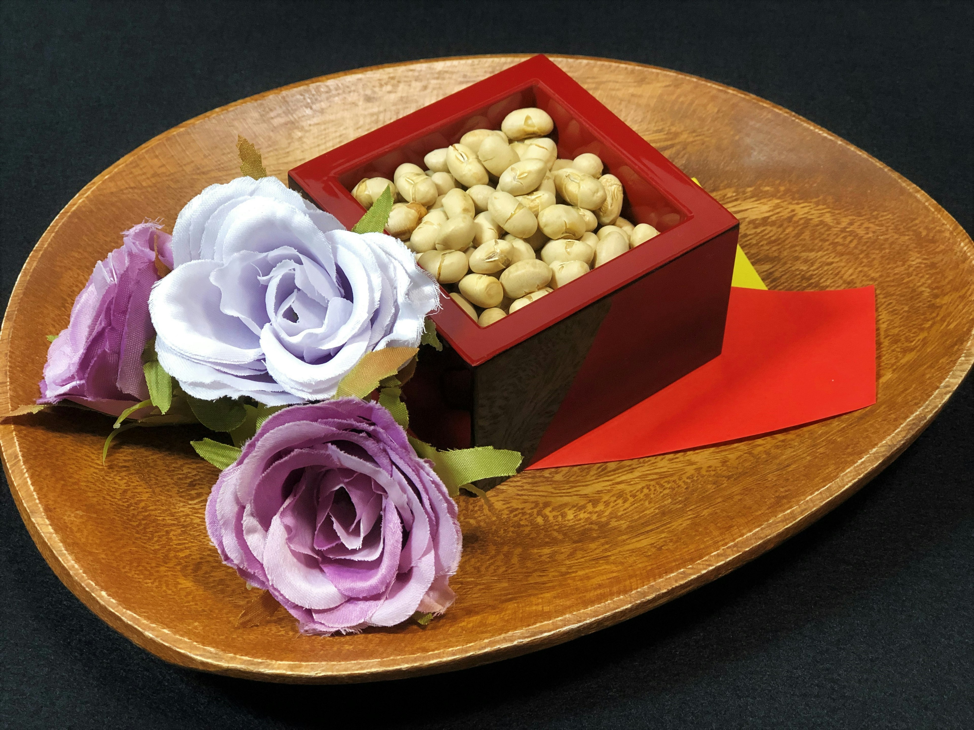 Plato de madera con una caja roja llena de frijoles y flores moradas