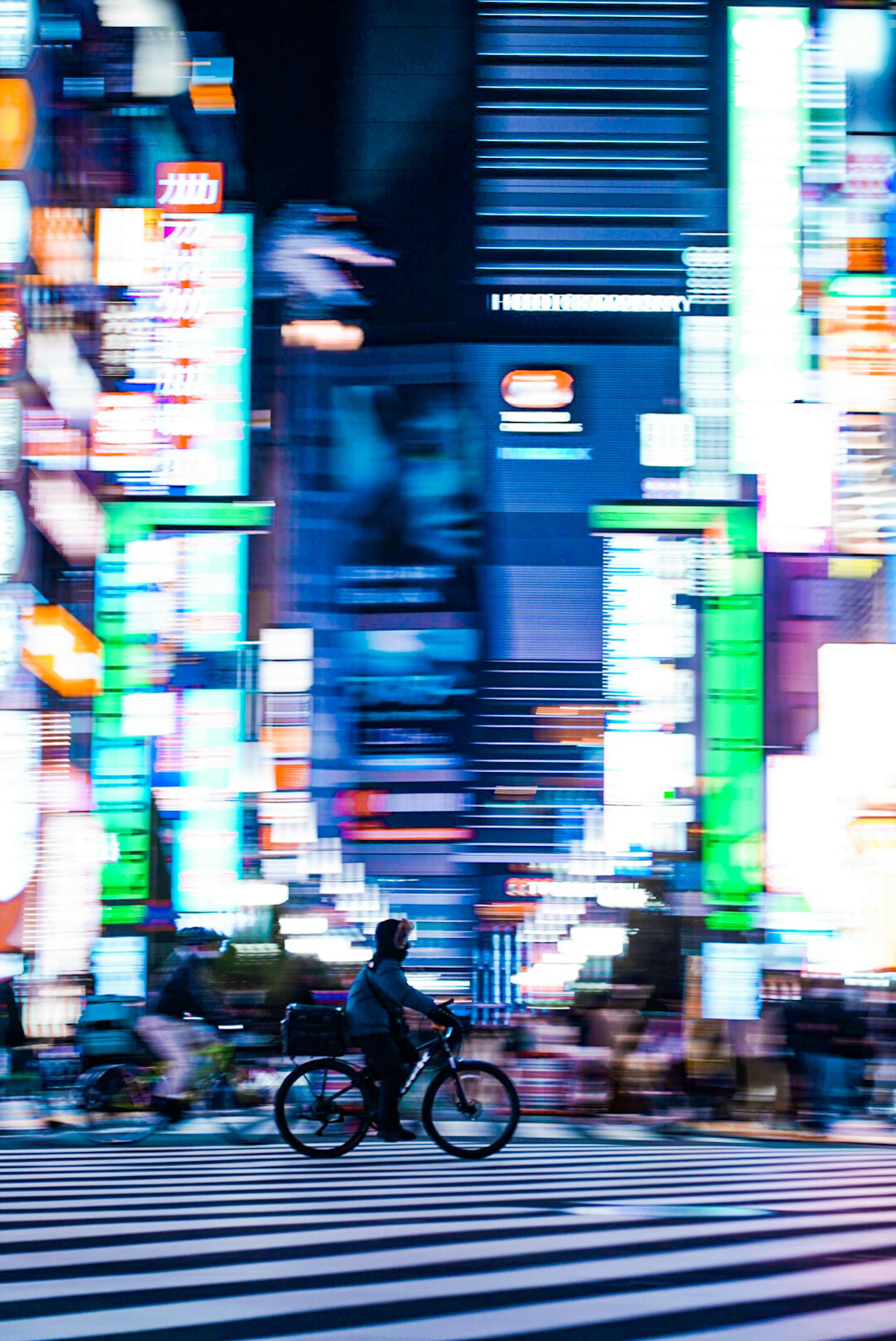 夜の街を自転車で走る人物と色とりどりのネオンの光