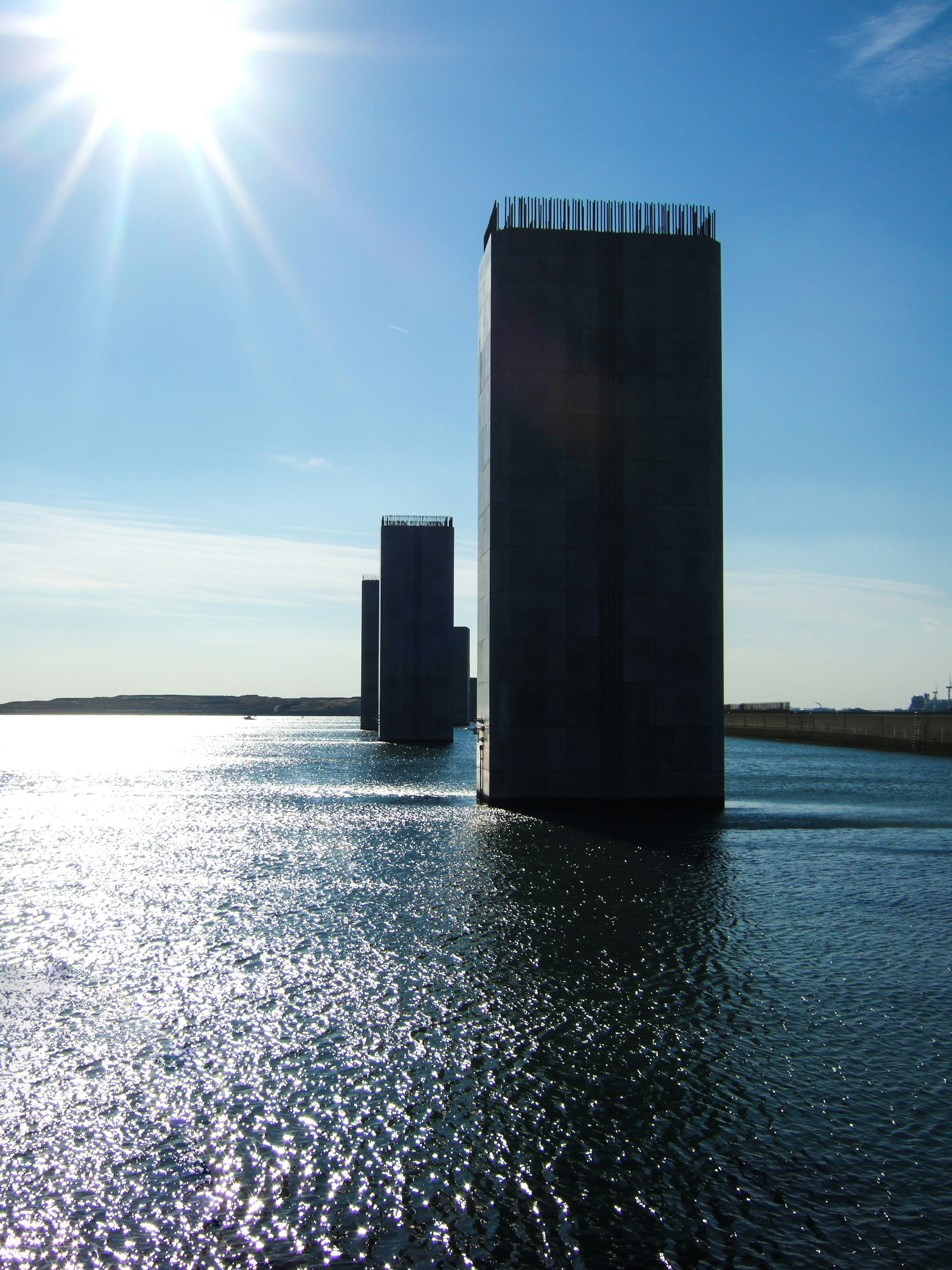 Landschaft mit drei Betonsäulen, die Sonnenlicht auf der Wasseroberfläche reflektieren