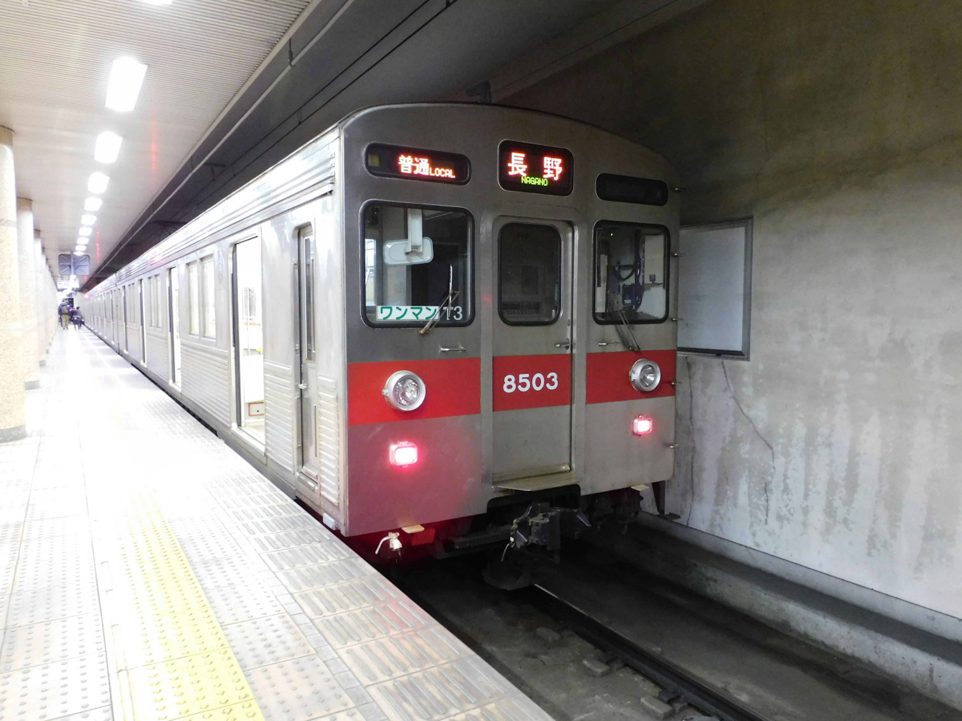 Tren de metro plateado con franjas rojas detenido en la estación