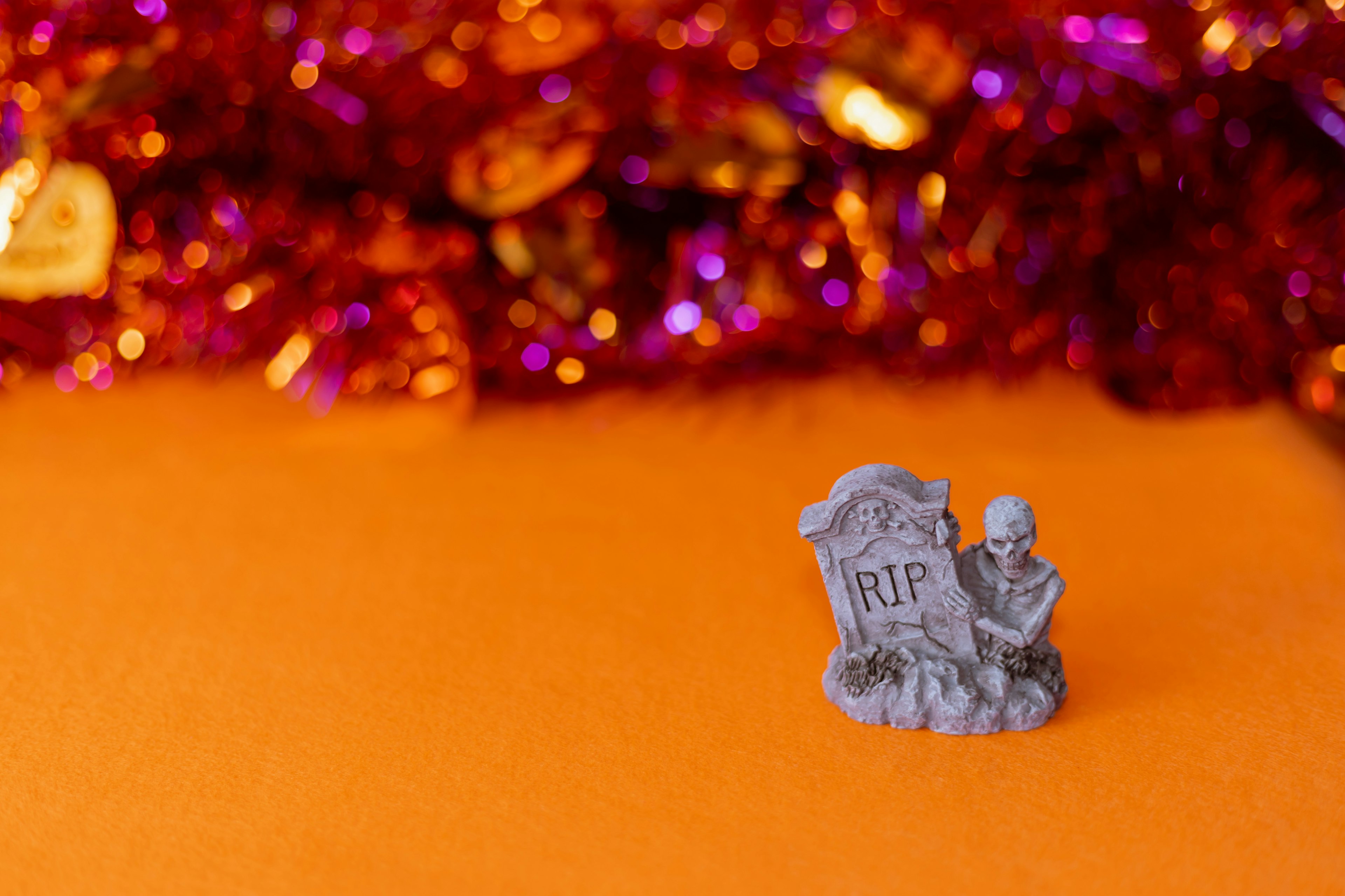 Miniature tombstone and gravekeeper figurine on an orange background