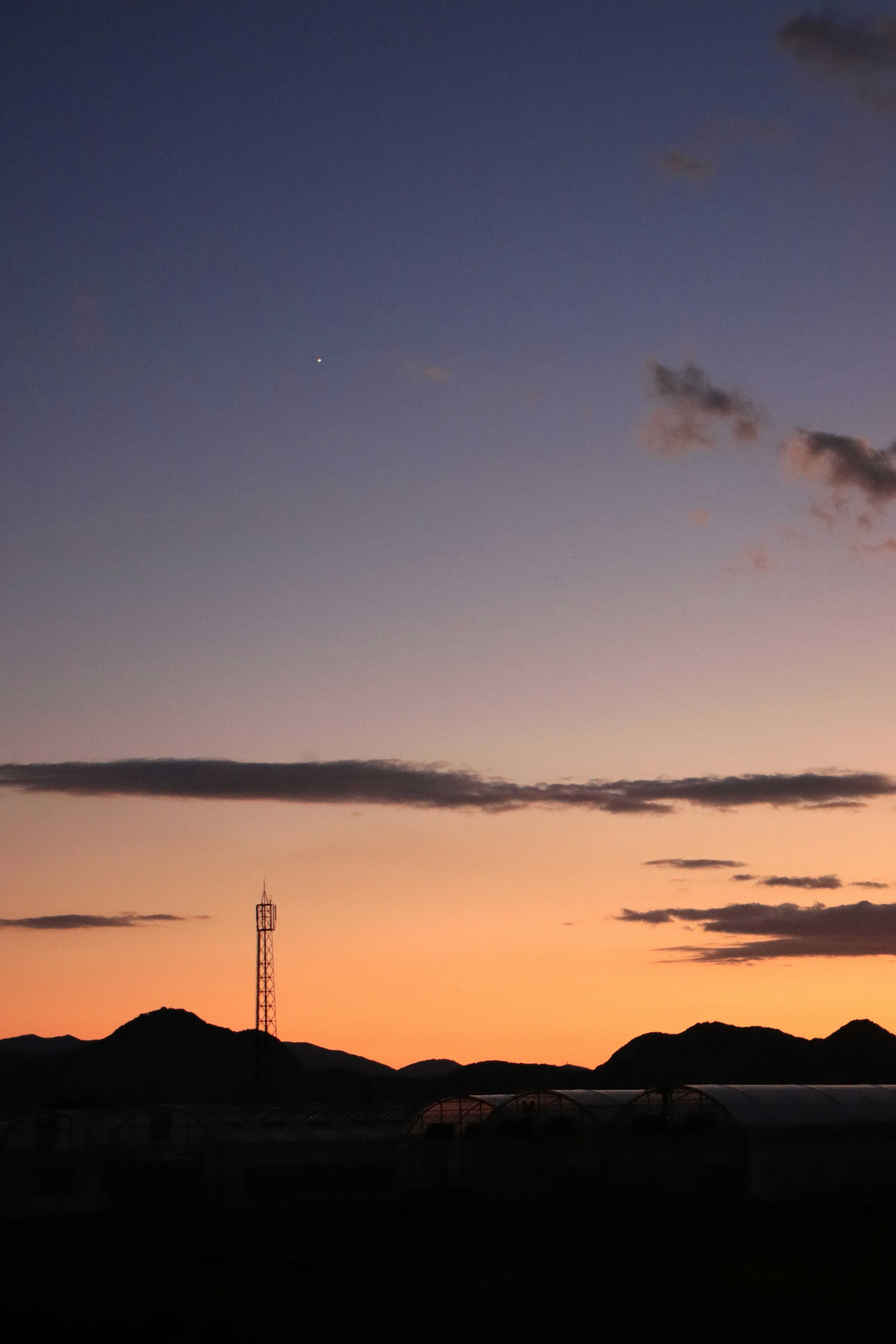 Pemandangan senja dengan langit gradasi oranye dan biru serta pegunungan dalam siluet