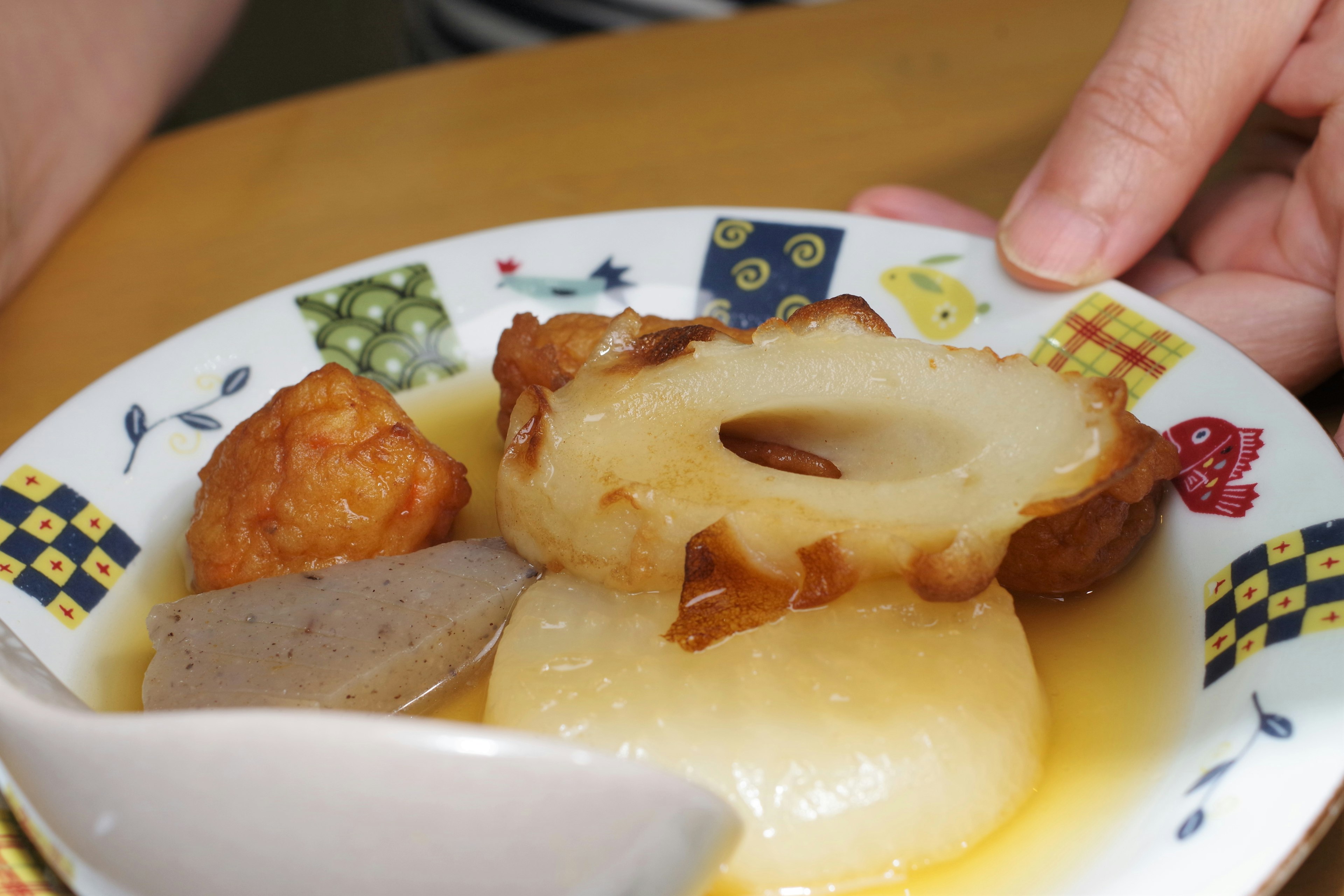 A bowl of simmered dishes with various ingredients and a hand