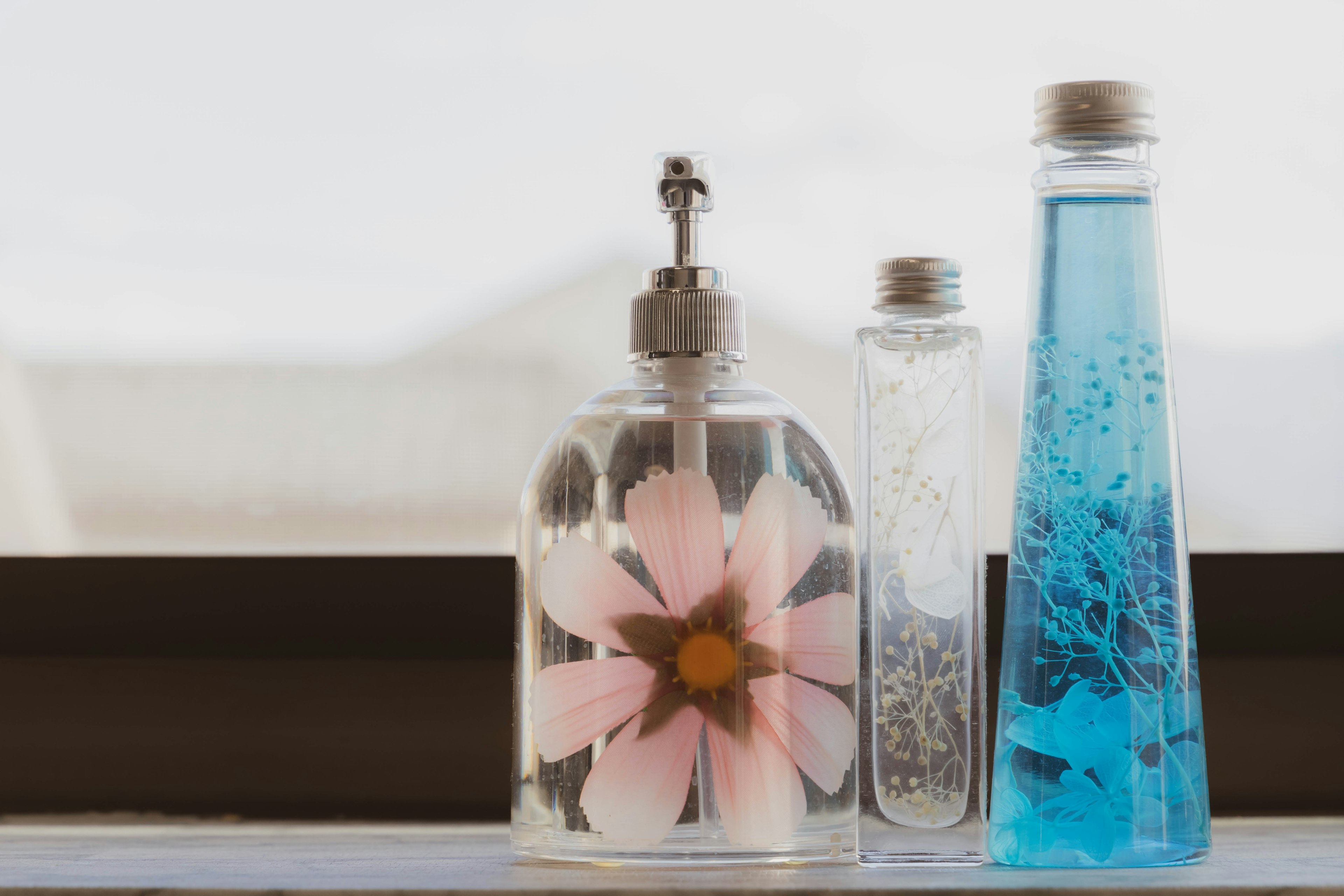 Three decorative bottles on a windowsill featuring a flower design and blue liquid