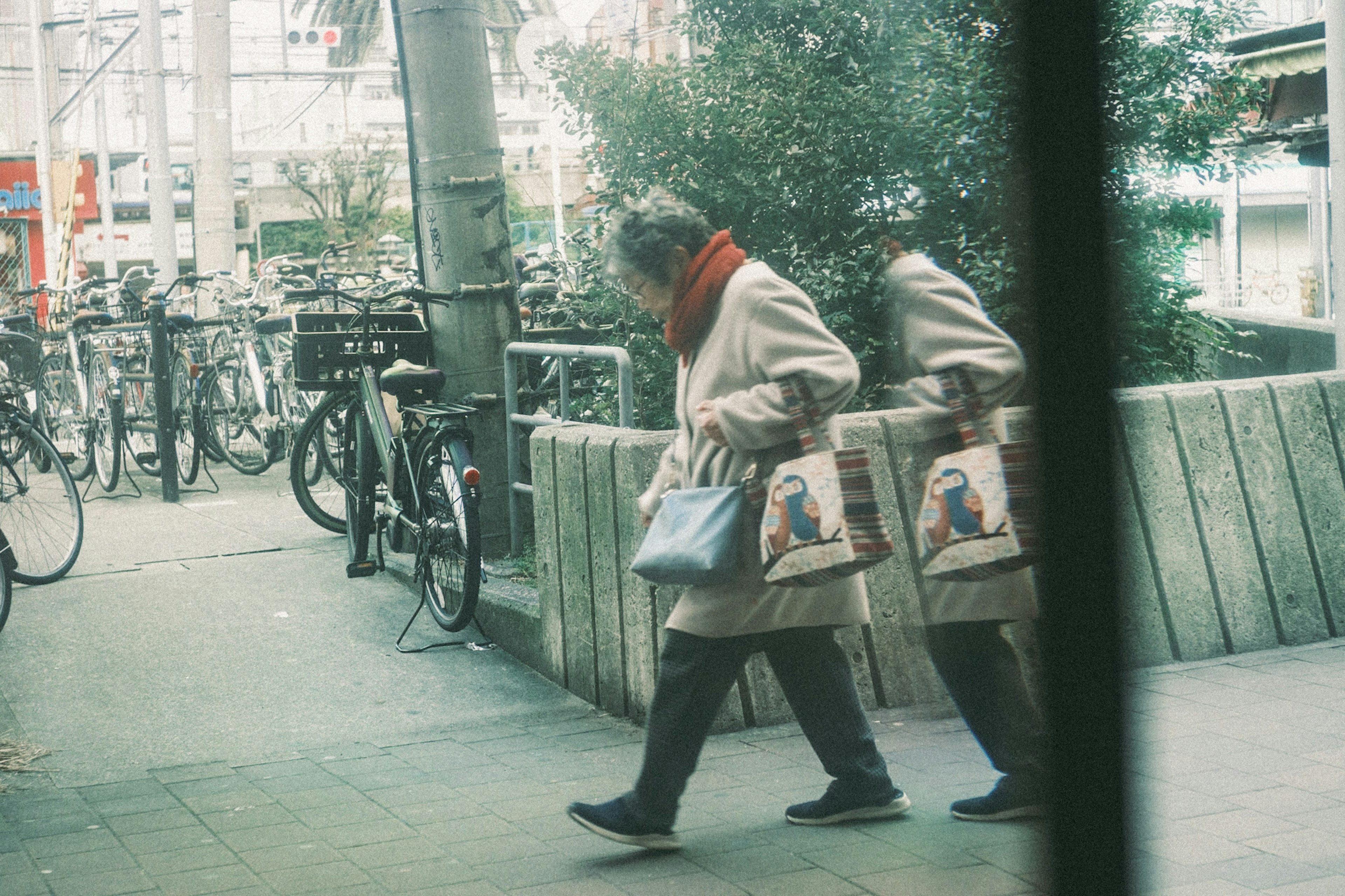 赤いスカーフを巻いた女性が買い物袋を持って歩いている様子周囲には自転車が並んでいる