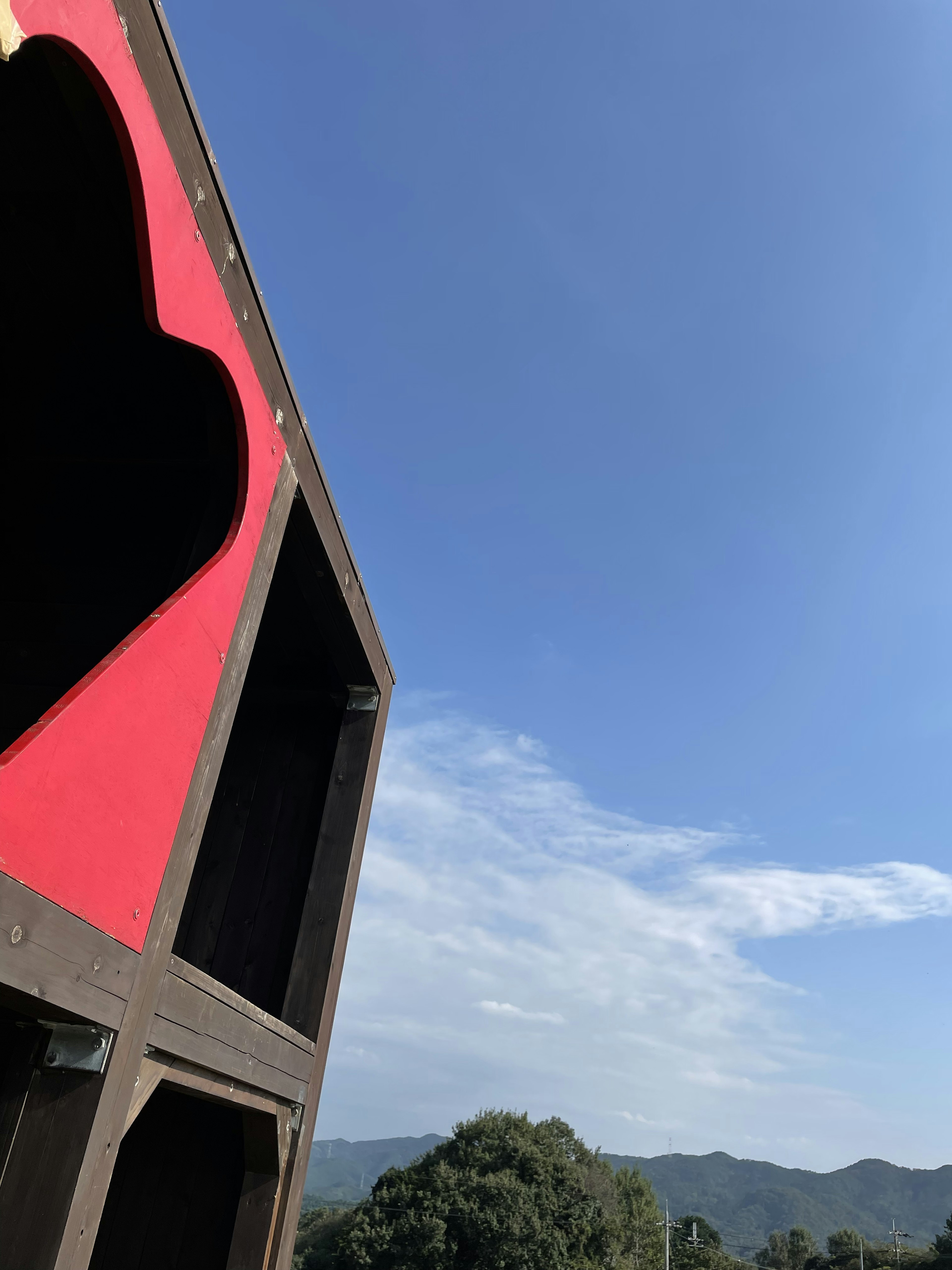 Estructura de madera con una ventana en forma de corazón rojo contra un cielo azul