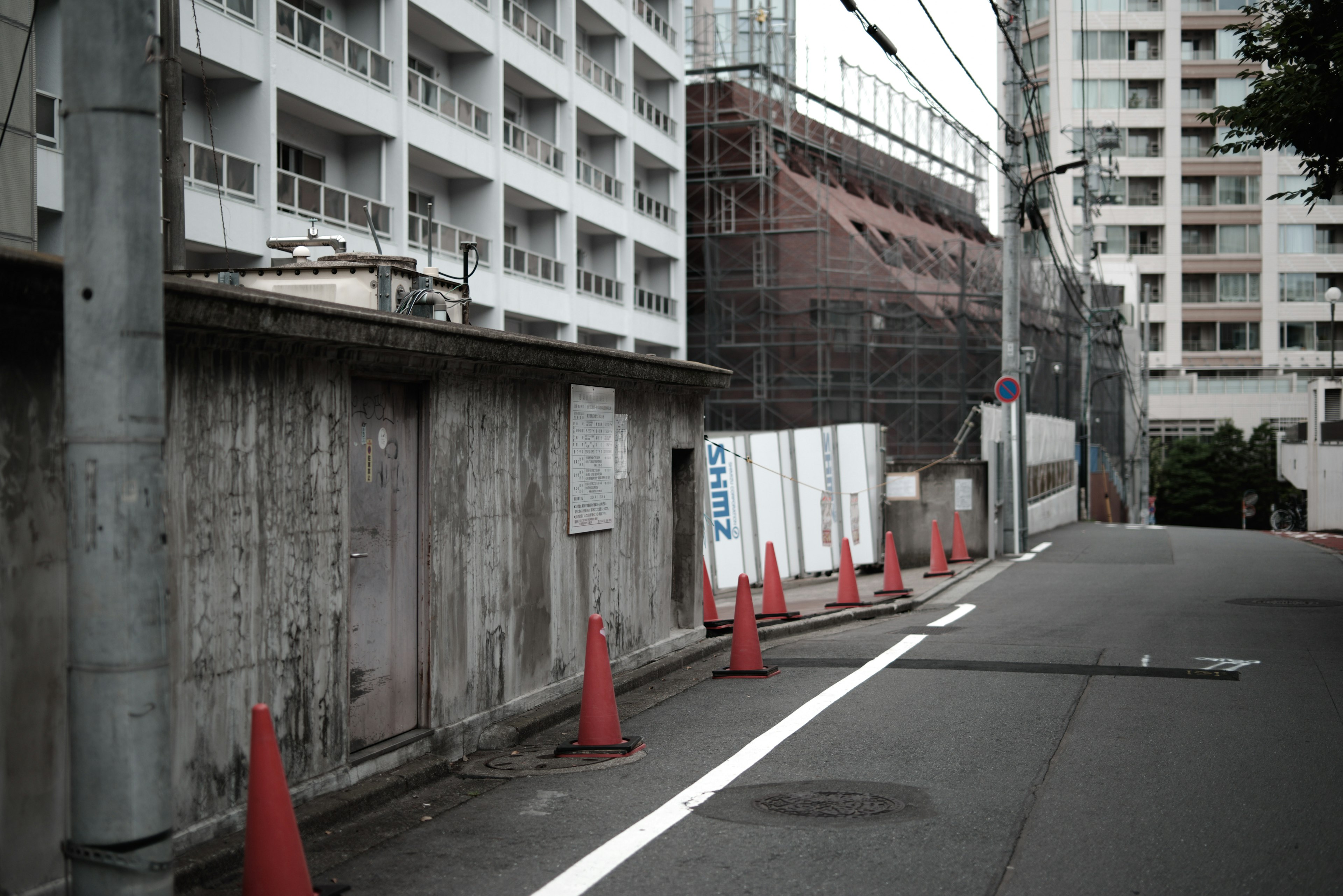 建設中のビルとコンクリート壁がある通りの風景 赤いコーンが配置されている