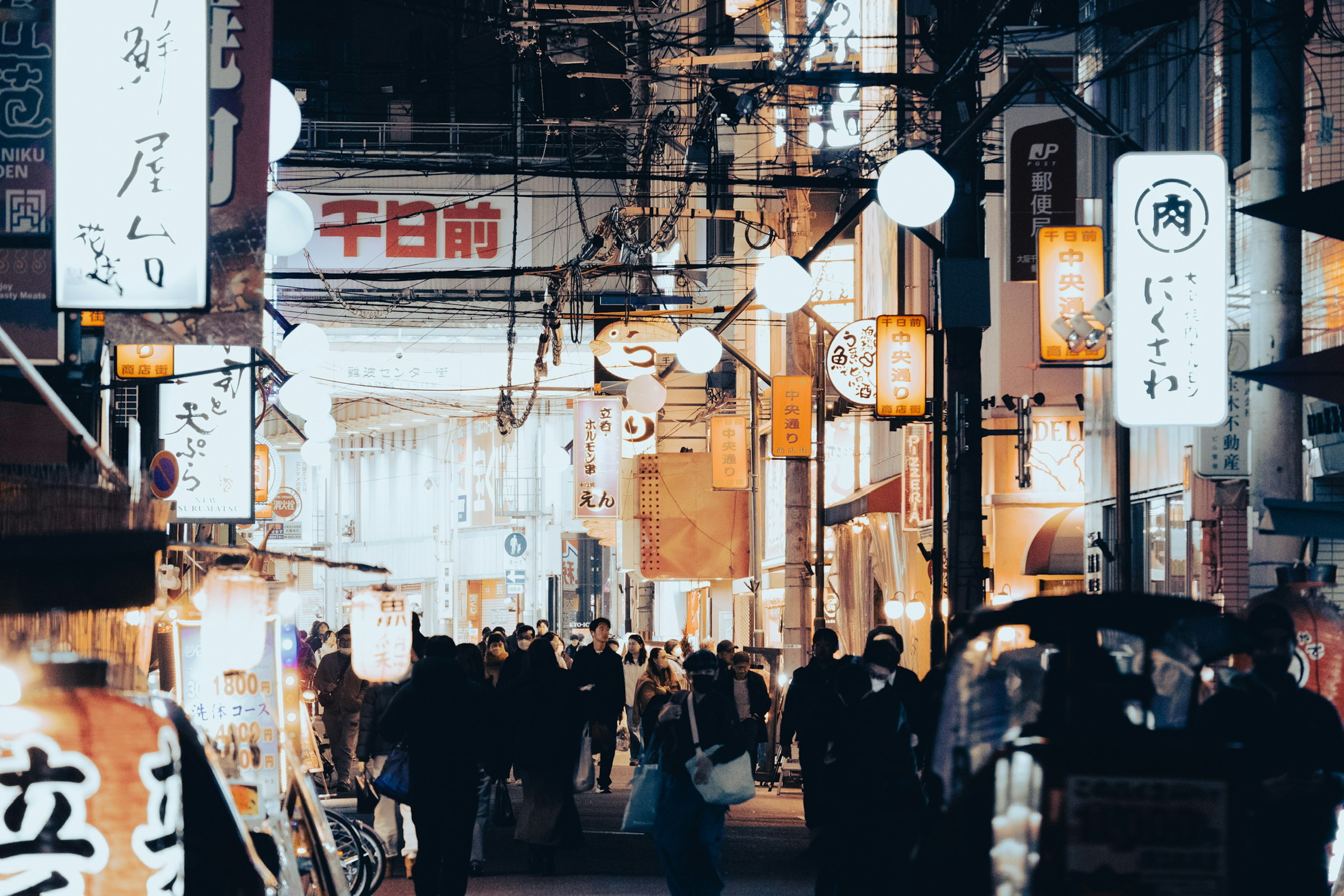 Belebte Straße mit Menschen und Essensständen, beleuchtet von Laternen und Schildern