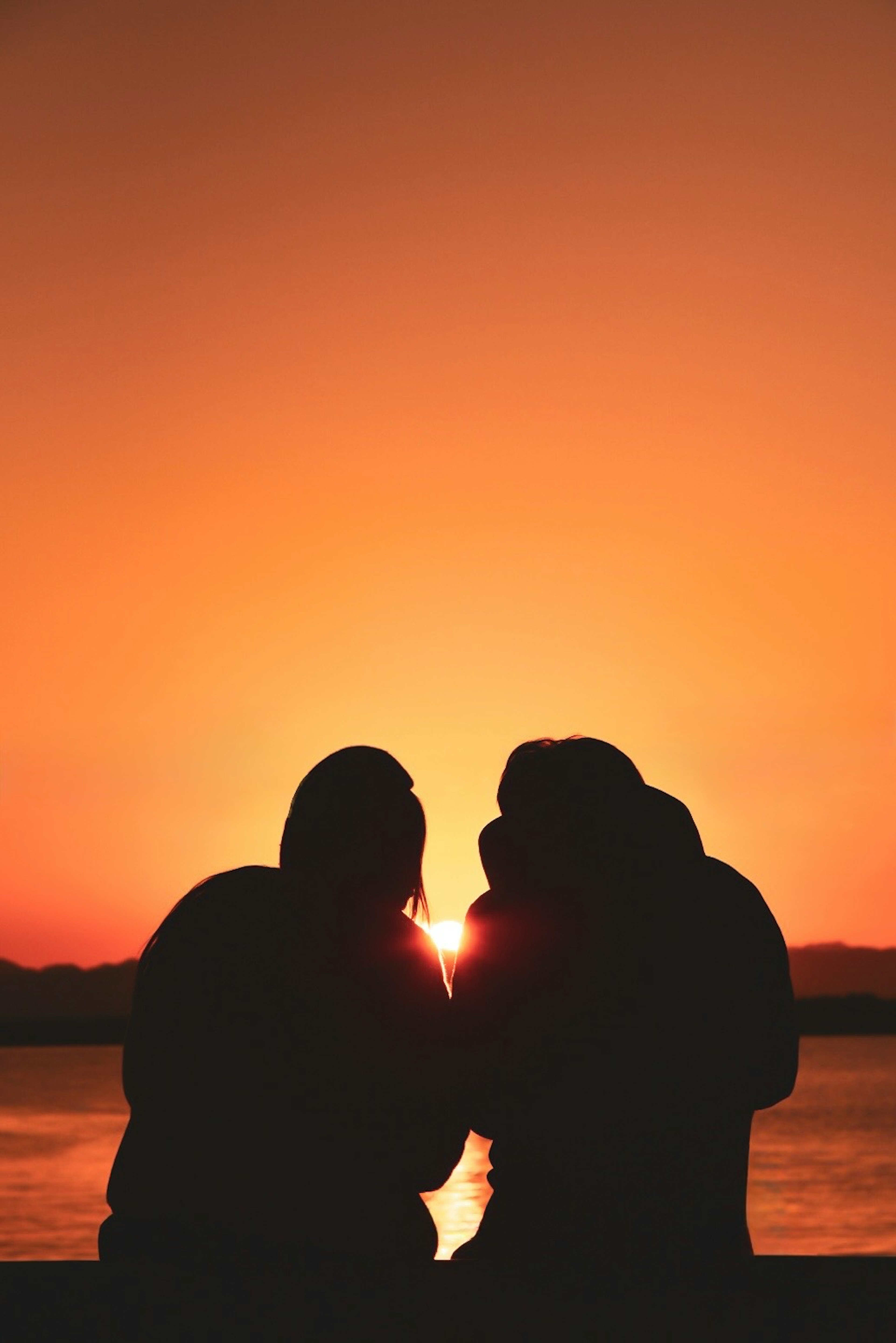 Silhouette of three people embracing against a sunset