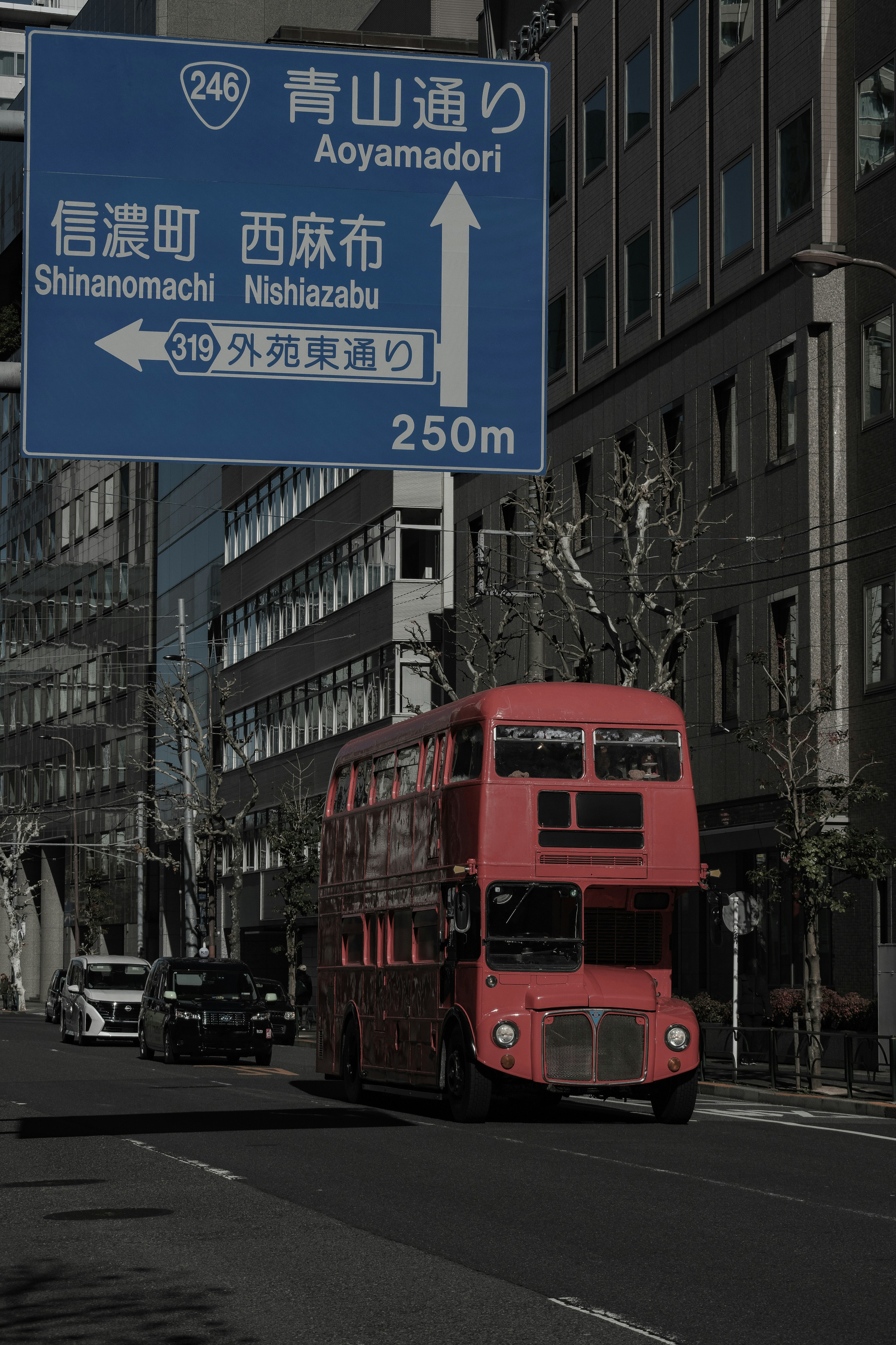 Red double-decker bus in urban setting with blue road sign