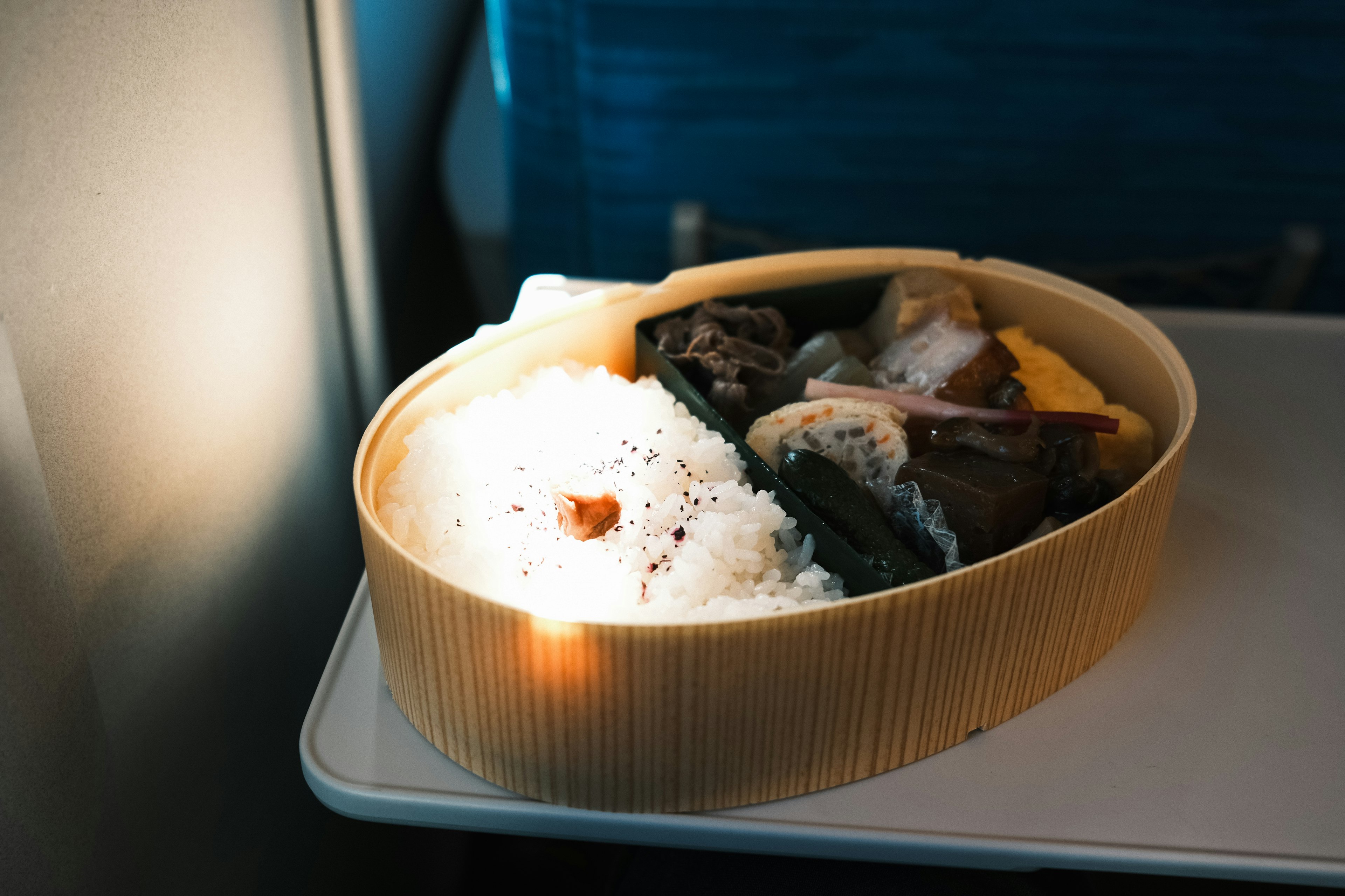 Bento box with rice and side dishes on an airplane tray