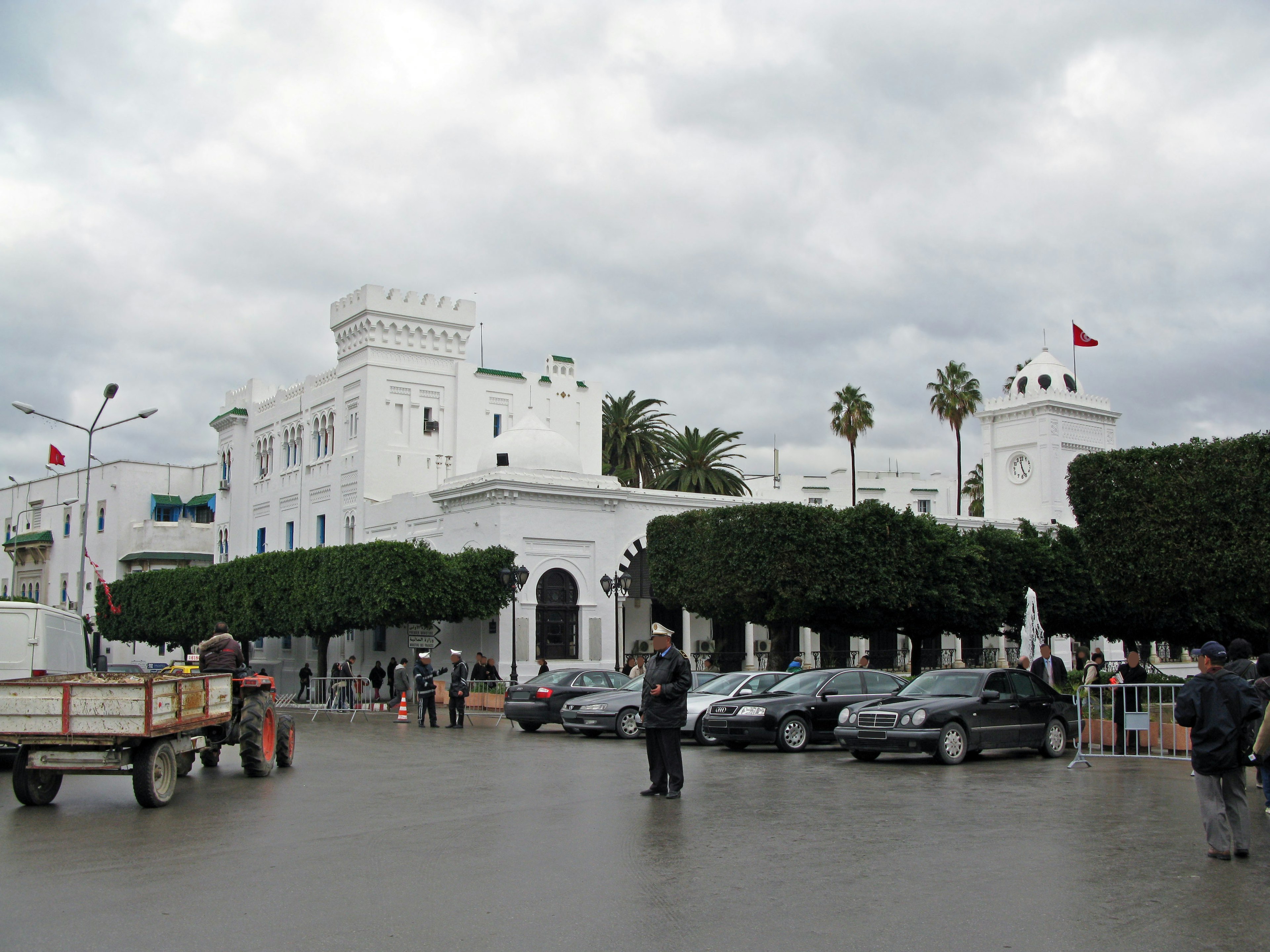 Alun-alun dengan bangunan putih dan pohon palem yang ada orang