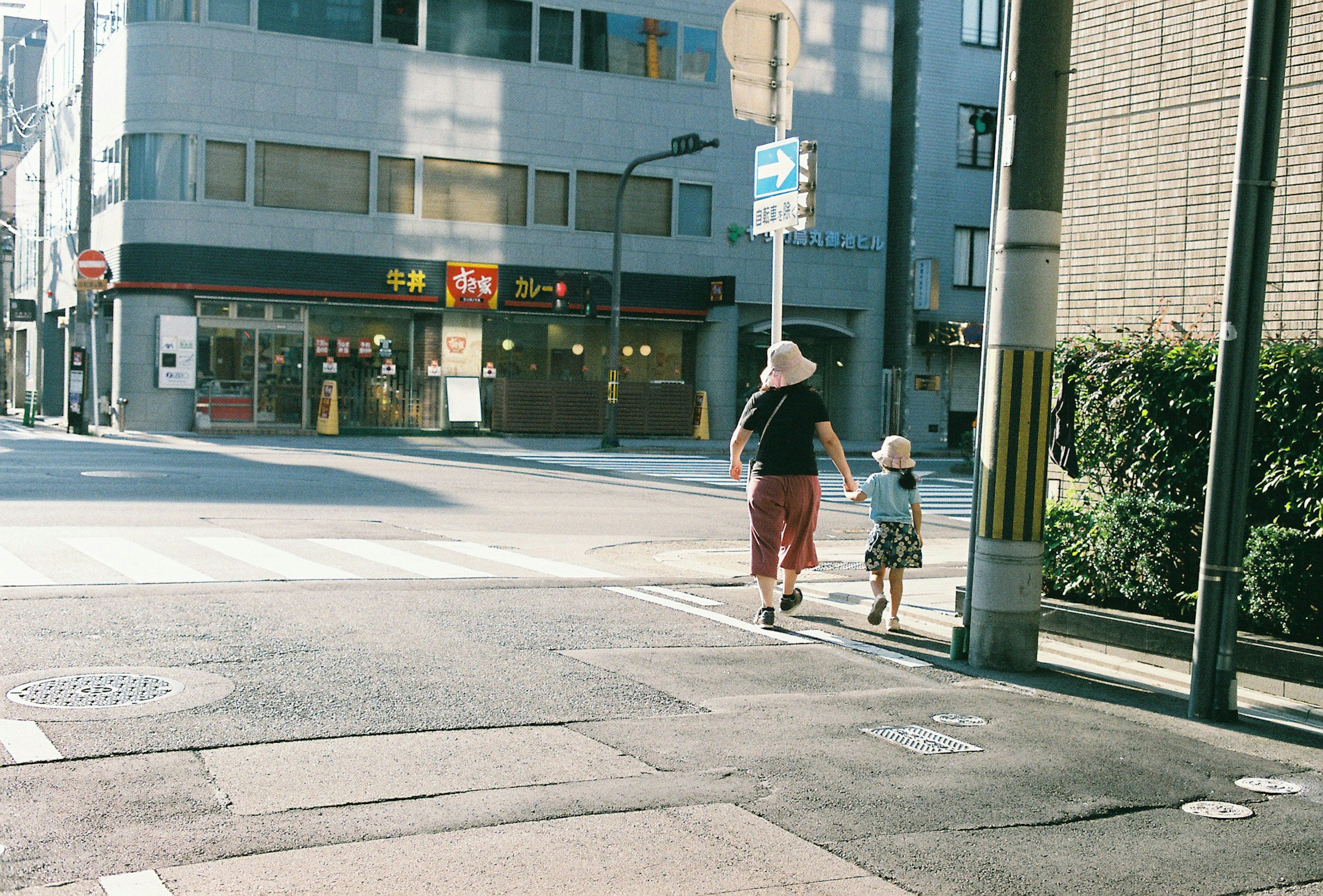 An adult wearing a large hat and a small child holding hands walking in a city street