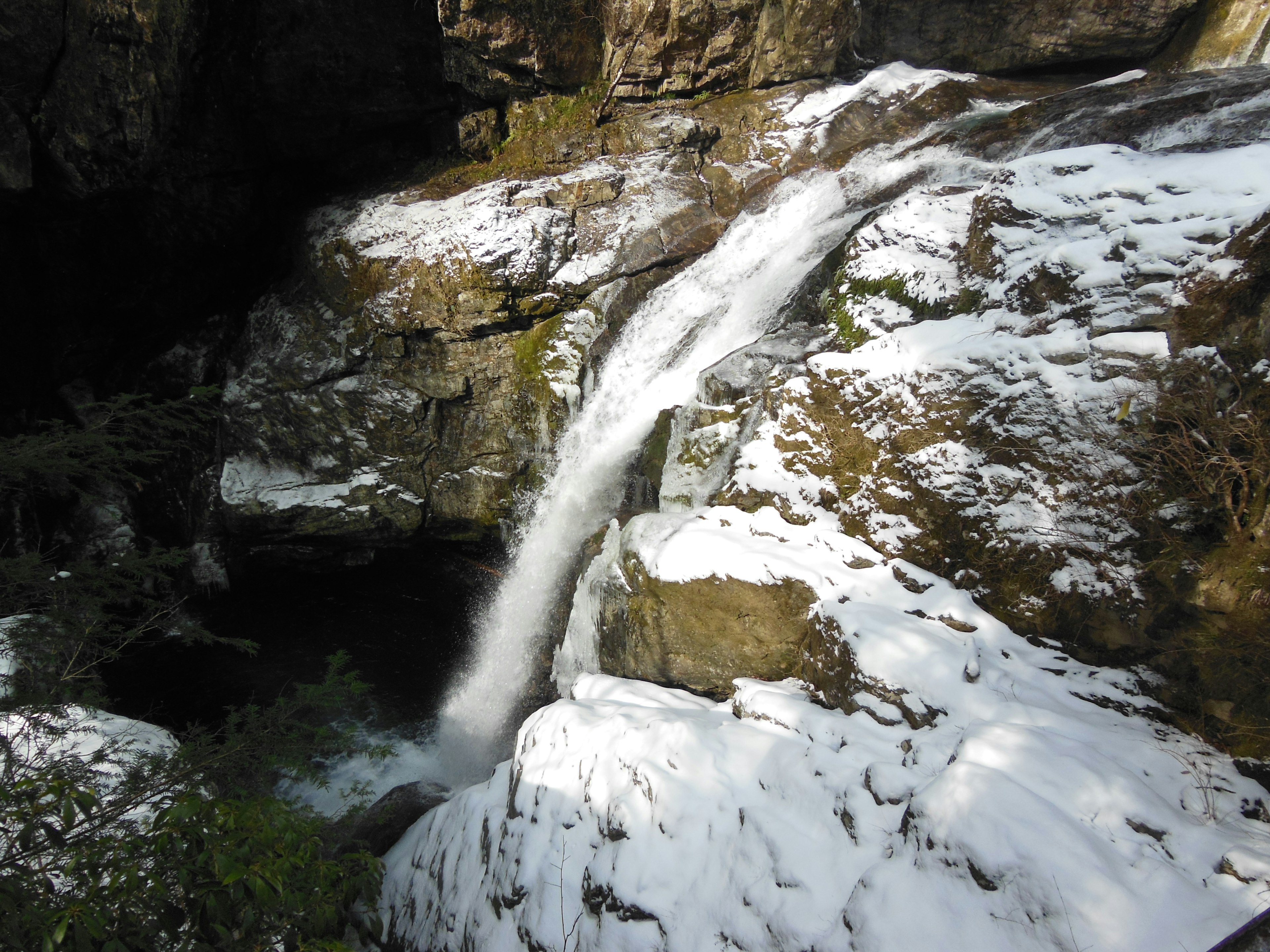 Kleine Wasserfall, der zwischen schneebedeckten Felsen fließt