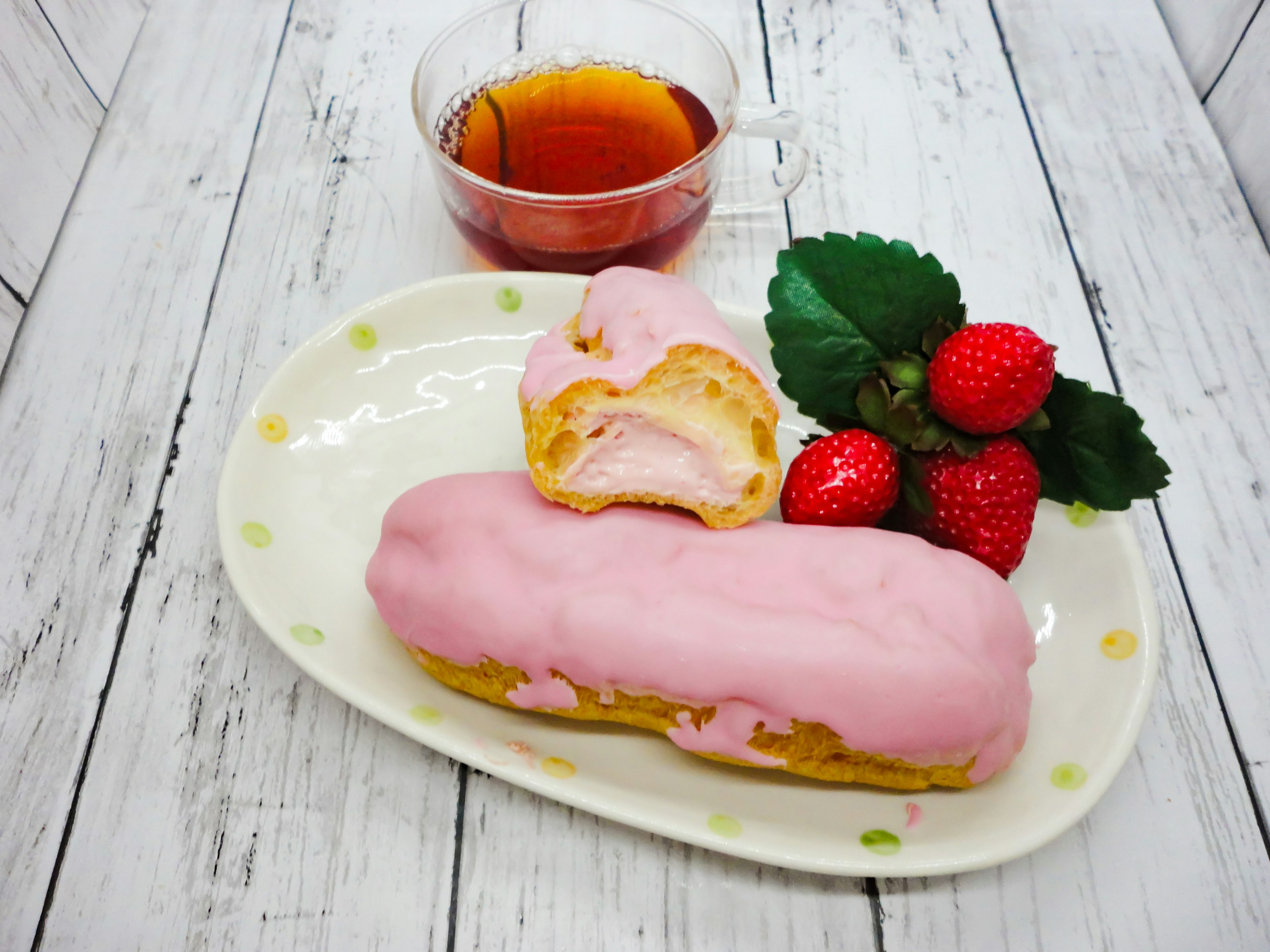 Un donut ripieno di crema con glassa rosa accanto a fragole fresche e una tazza di tè su un piatto