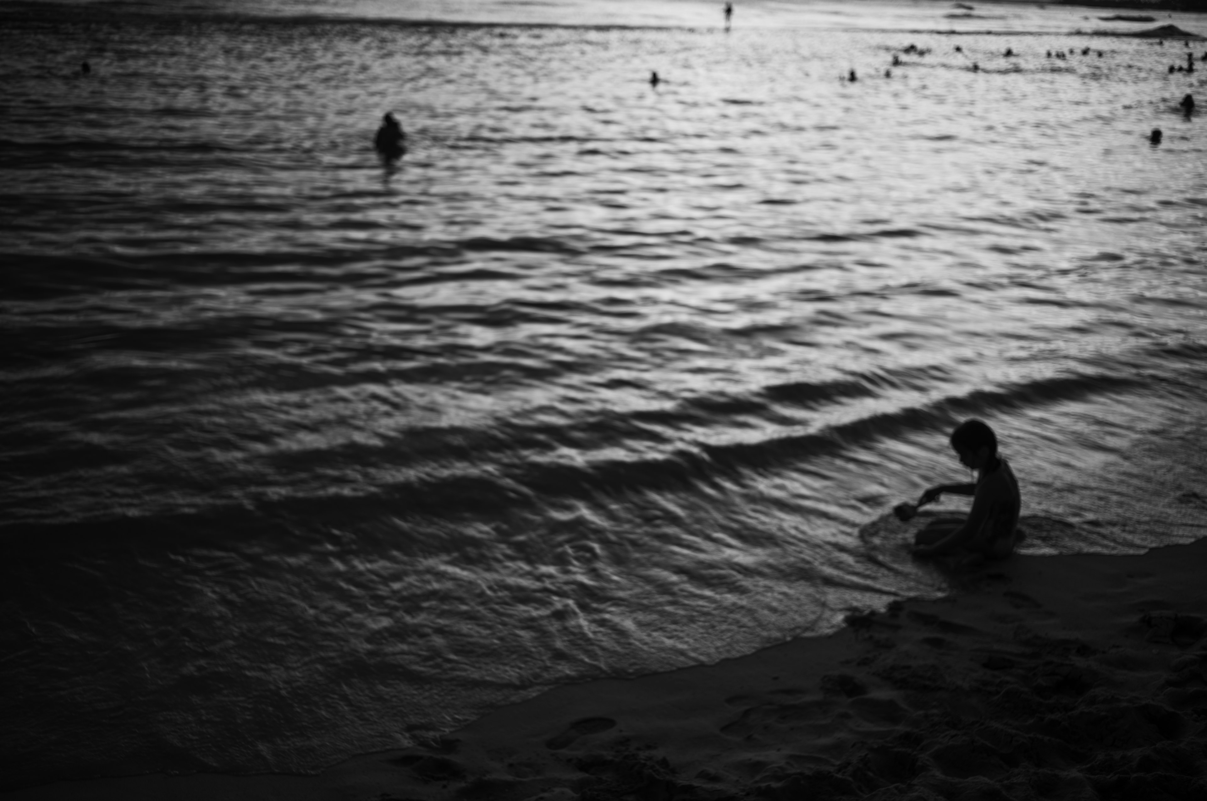 Kind, das am Strand mit Wellen in Schwarzweiß spielt