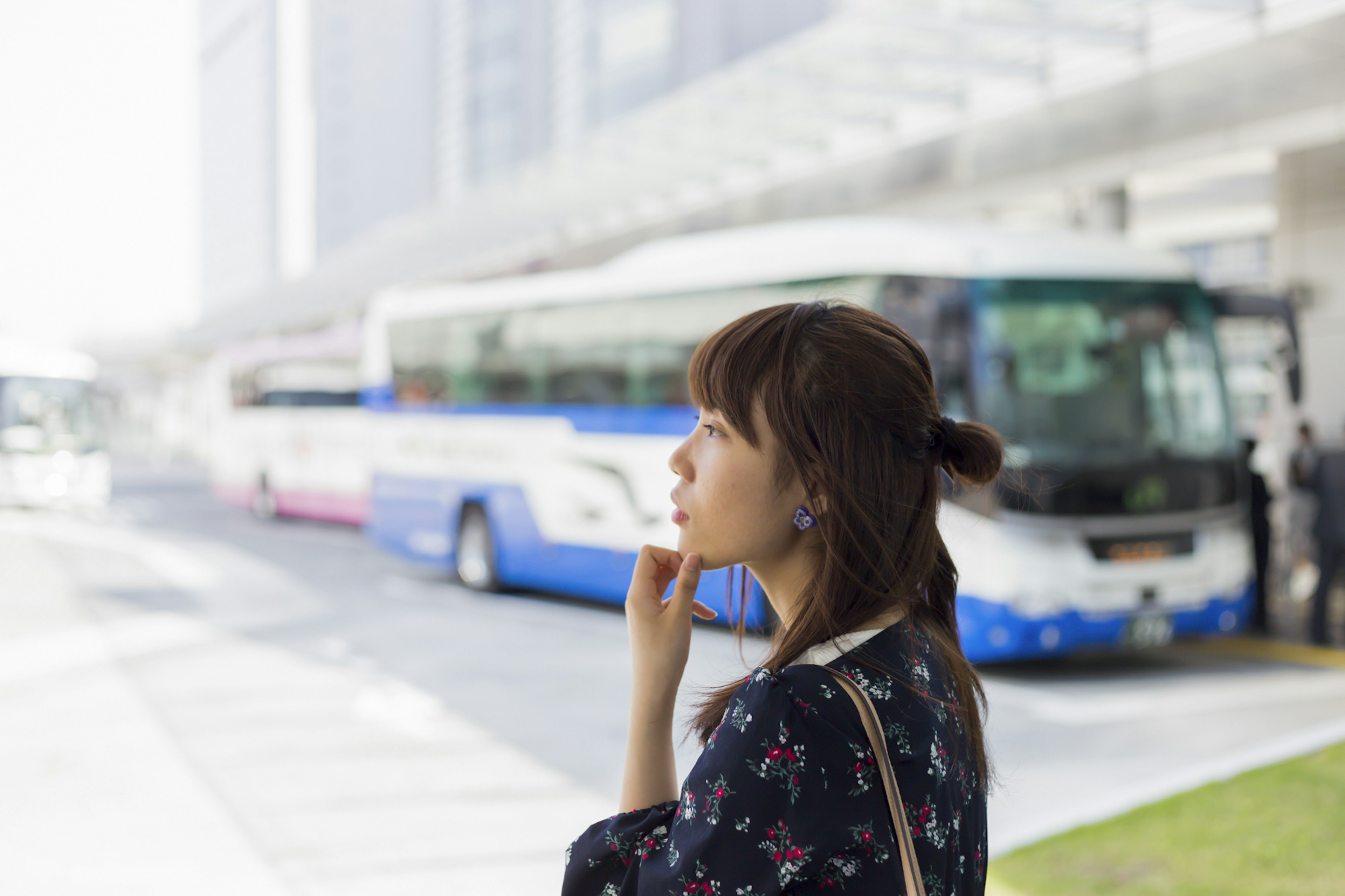 Une femme réfléchissant à un arrêt de bus avec des bus en arrière-plan et un cadre urbain