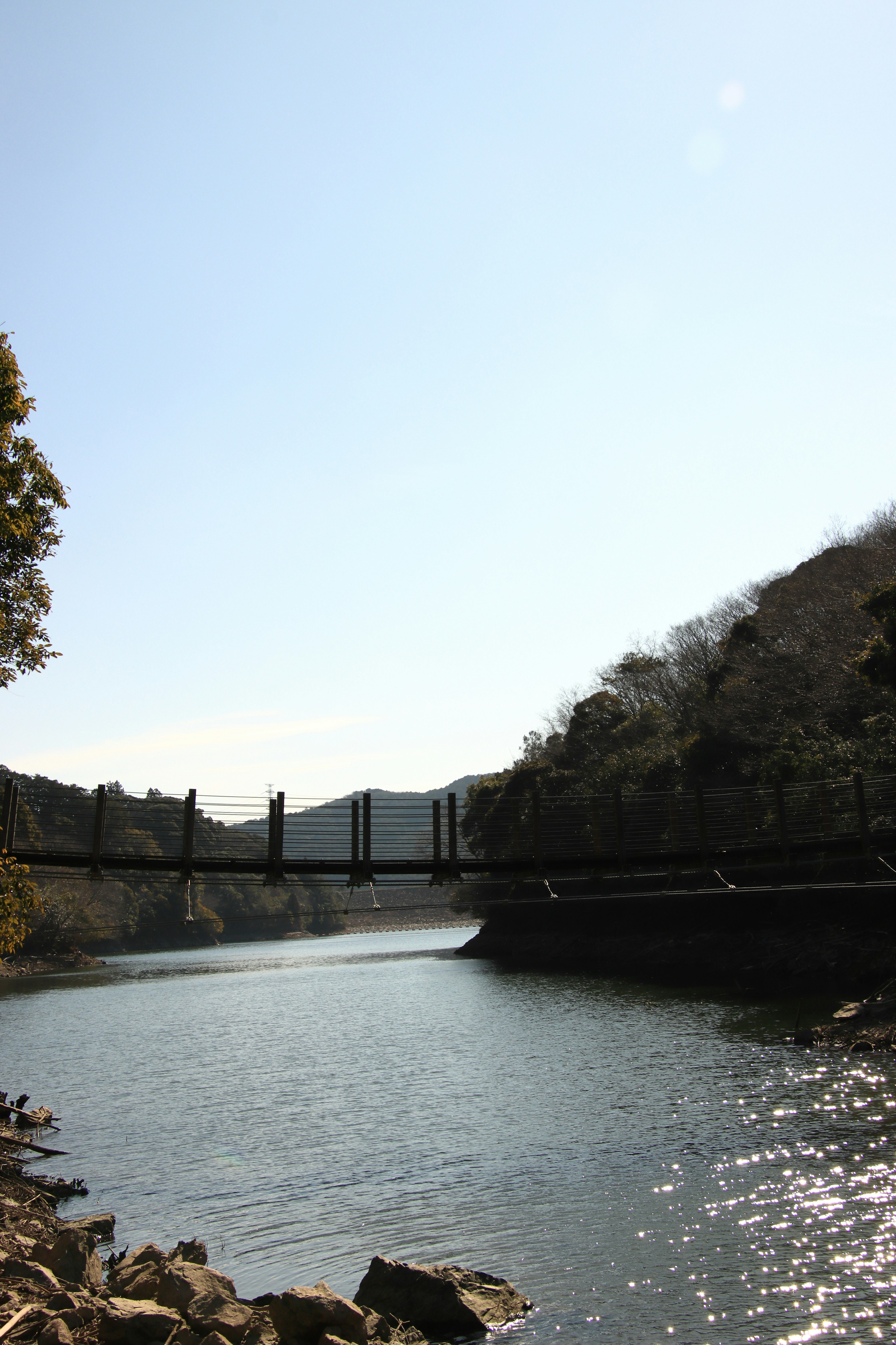 Suspension bridge over a calm river surrounded by mountains