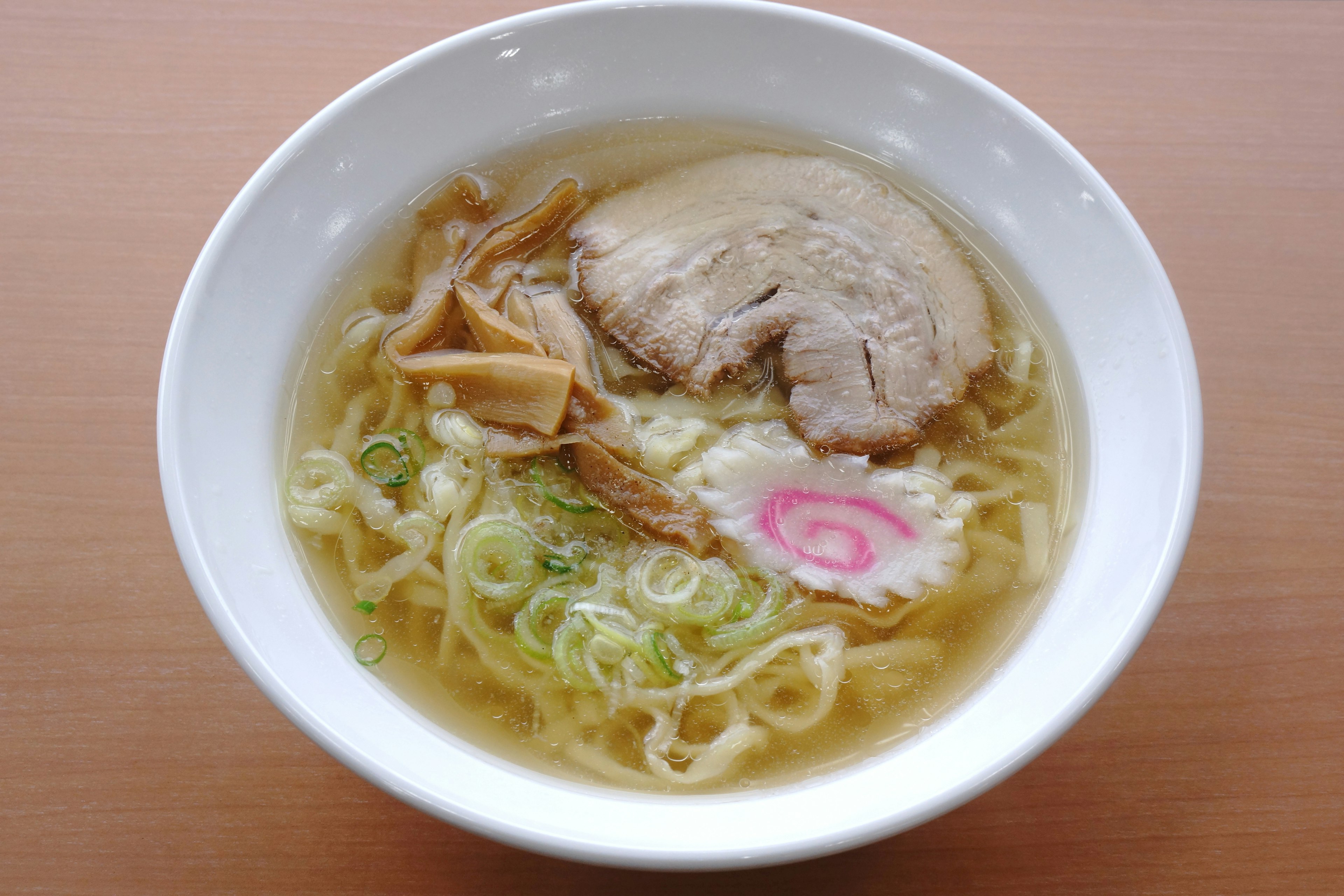 Mangkok ramen dengan irisan chashu, daun bawang, menma, dan narutomaki dalam kaldu bening