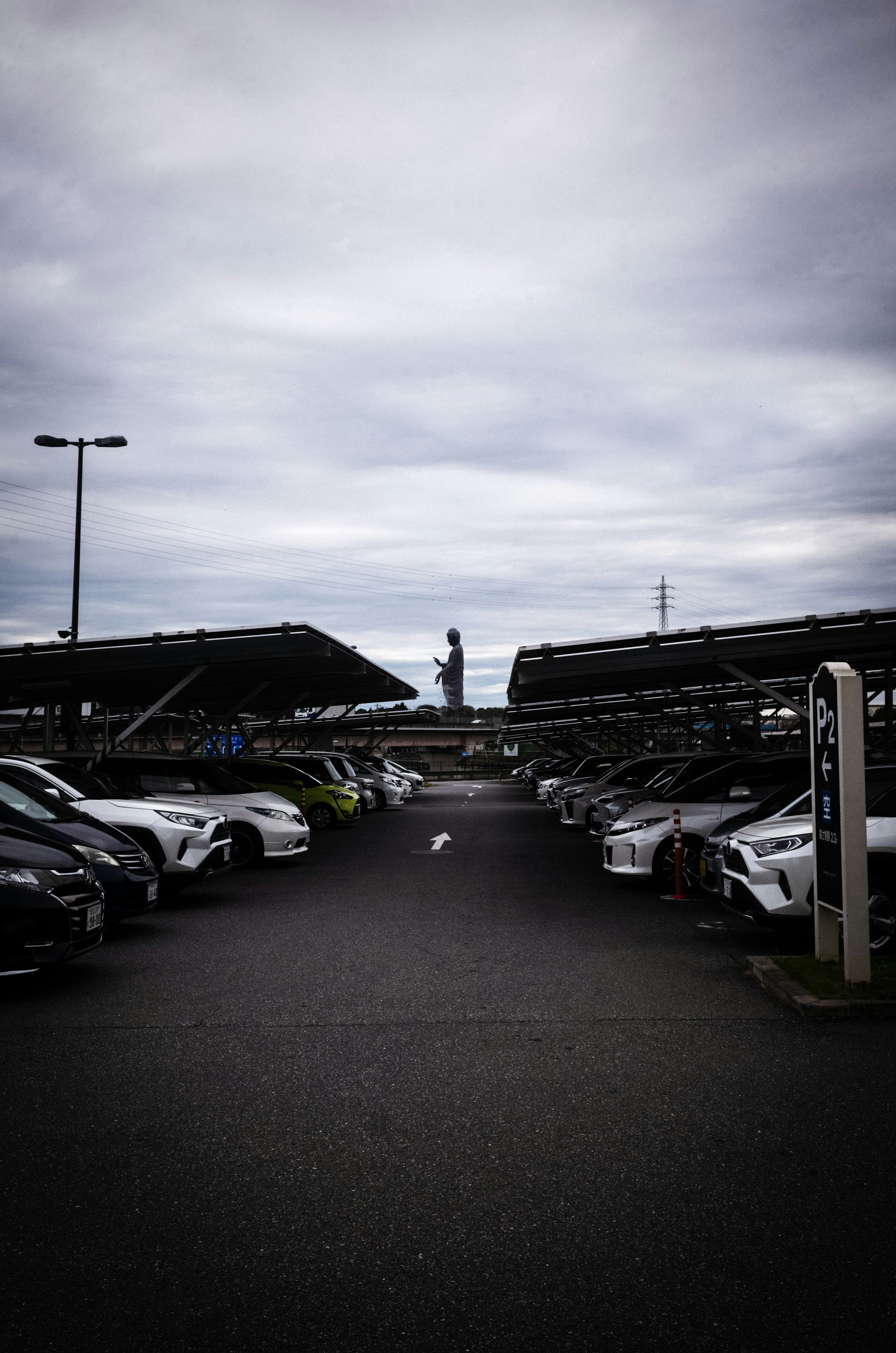 駐車場の中央に立つ人と並ぶ車両と曇った空