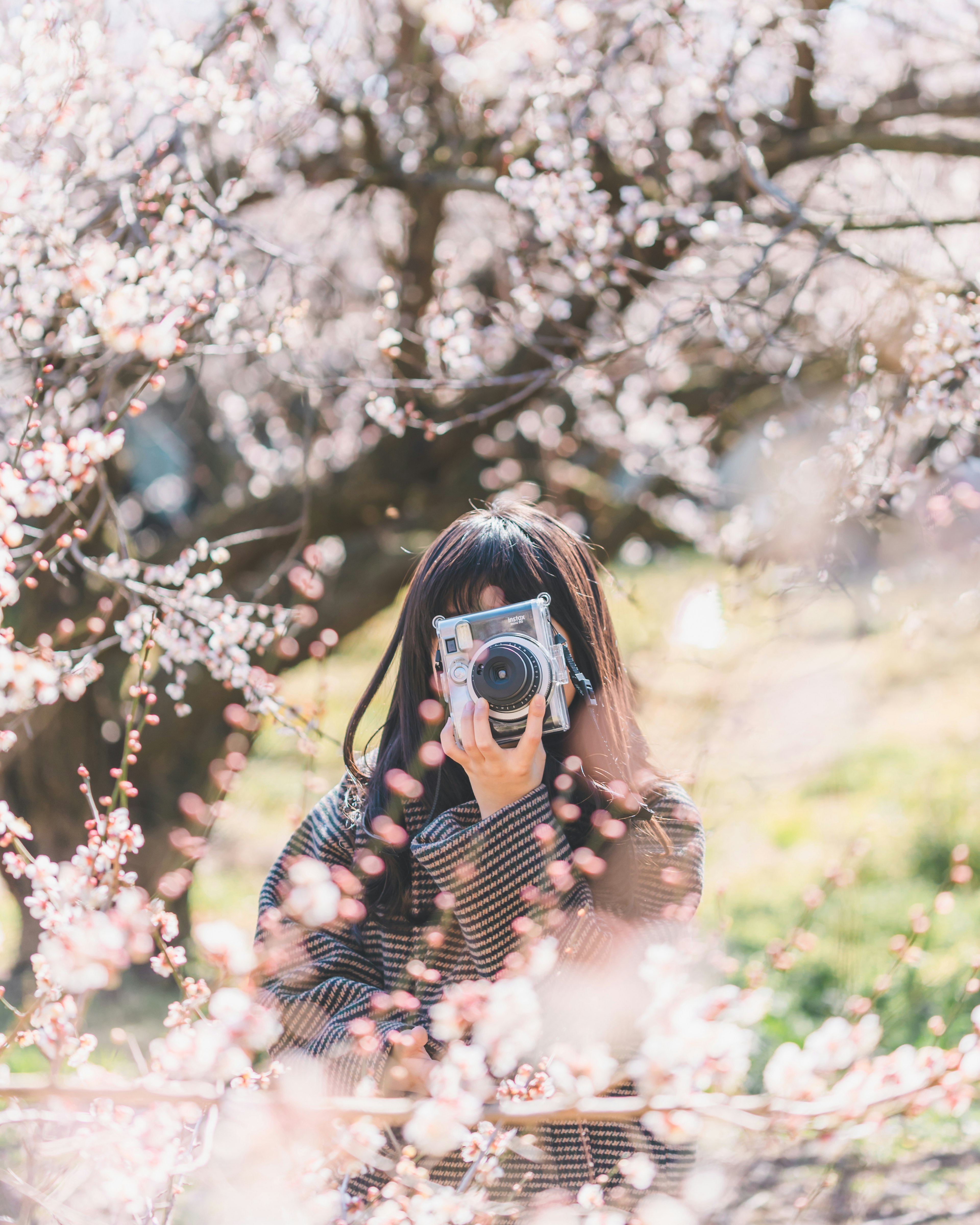 Seorang wanita memegang kamera di depan bunga sakura