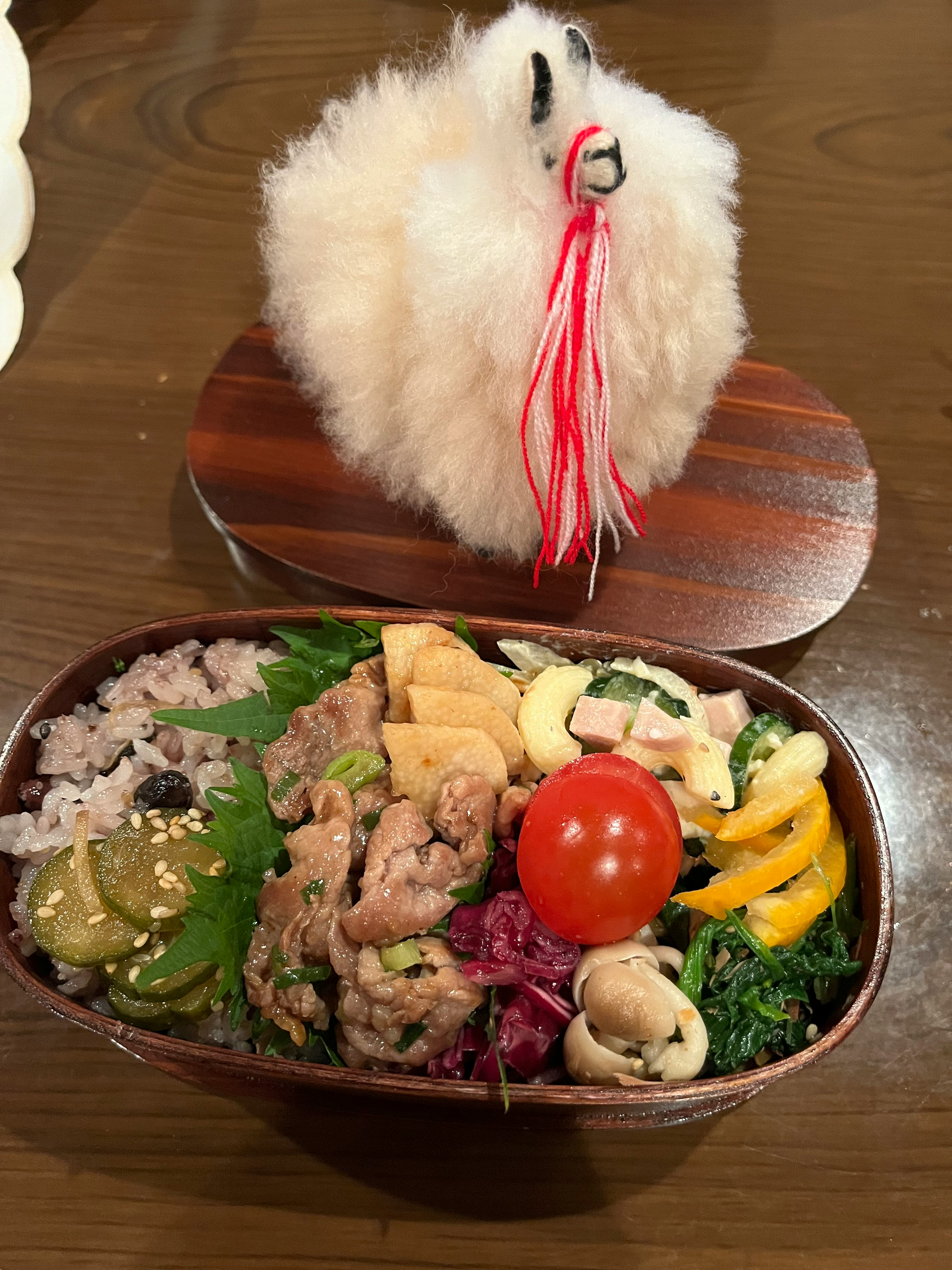 Une boîte à bento avec des ingrédients colorés placée sur une assiette en bois surmontée d'une décoration blanche duveteuse