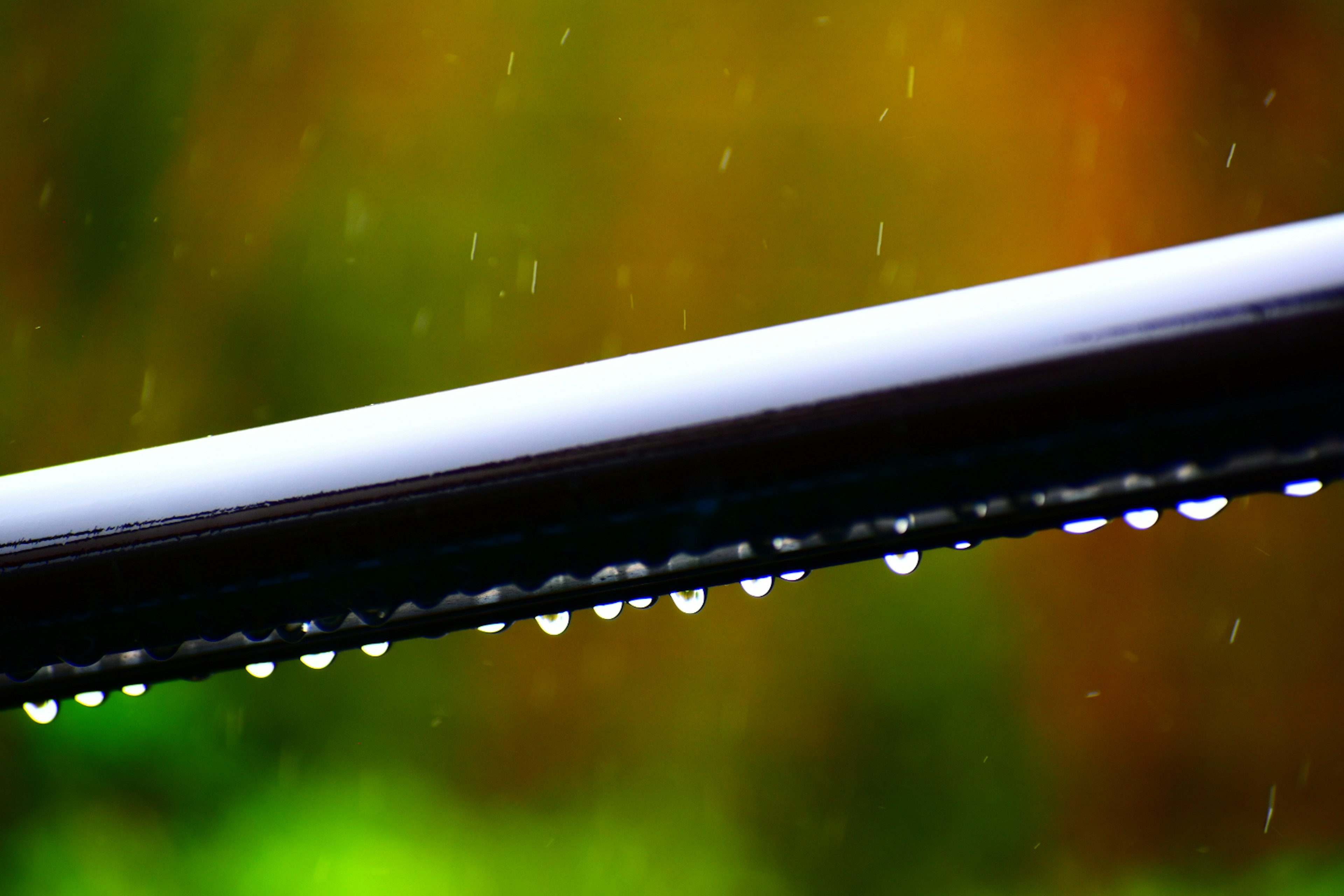 Close-up of a black bar with rain droplets and blurred colorful background