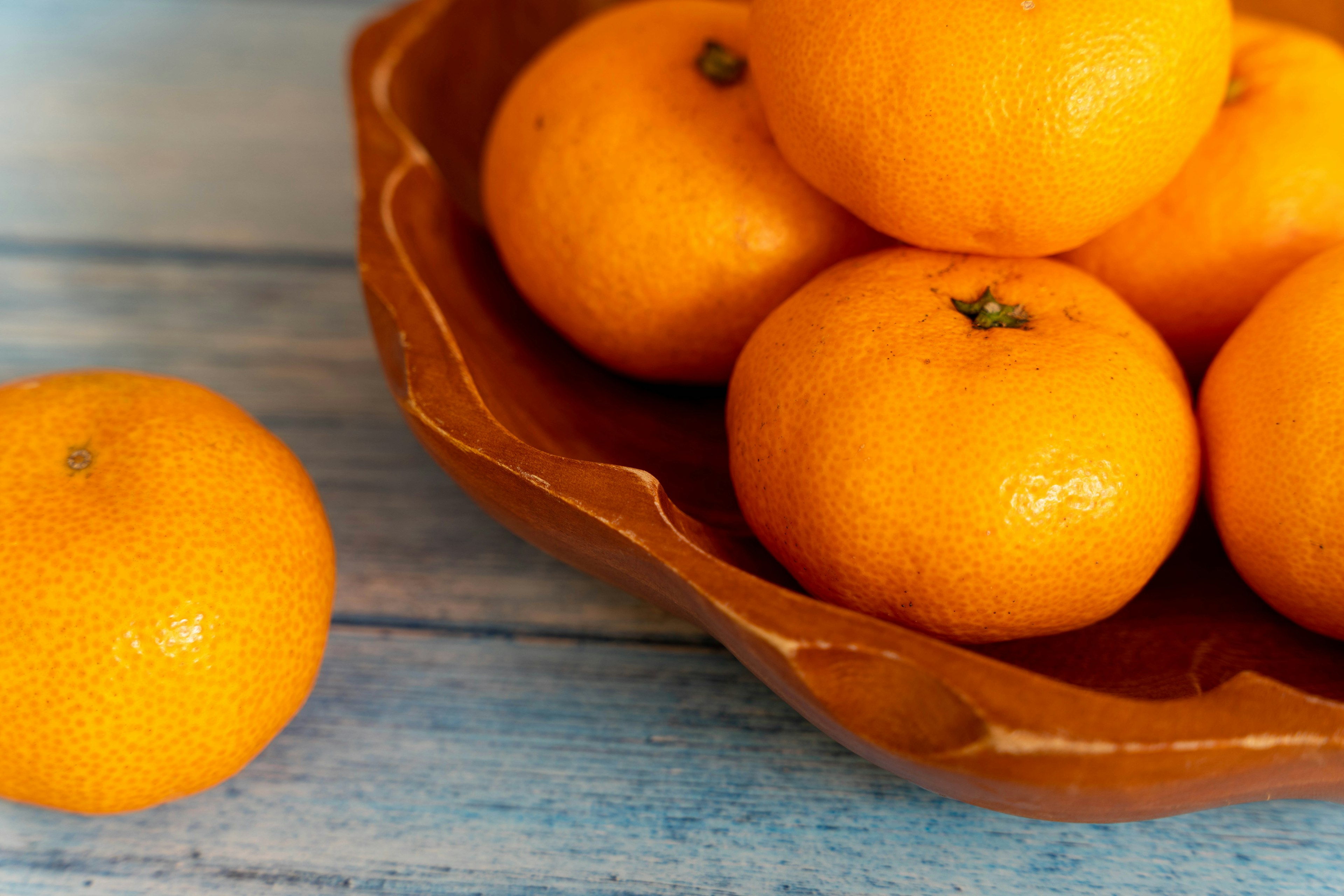 Wooden bowl filled with bright oranges on a blue wooden table