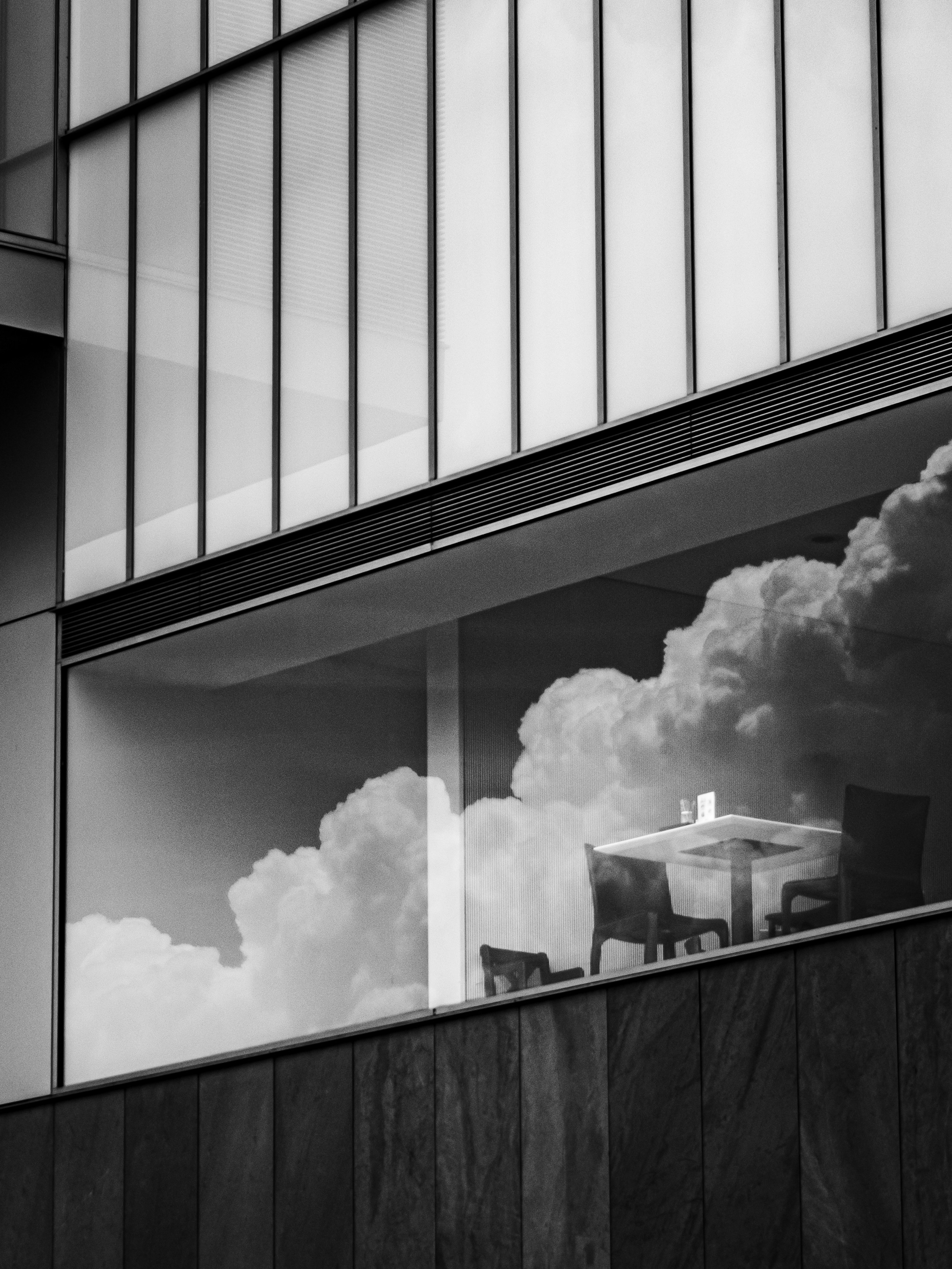 Une section de bâtiment moderne avec une fenêtre en verre montrant des nuages et une table