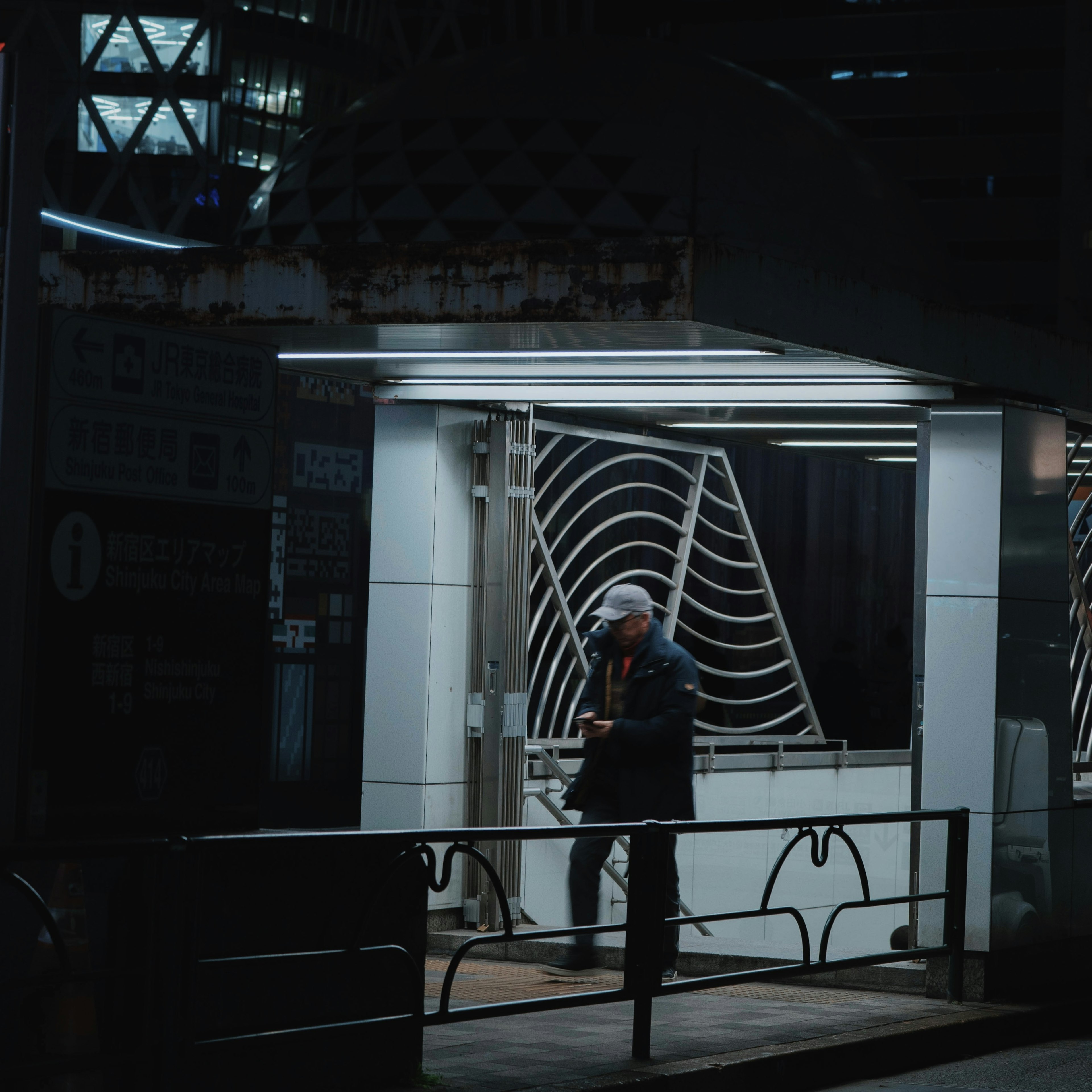 A bus stop at night with a person waiting illuminated by bright lights featuring a unique roof design