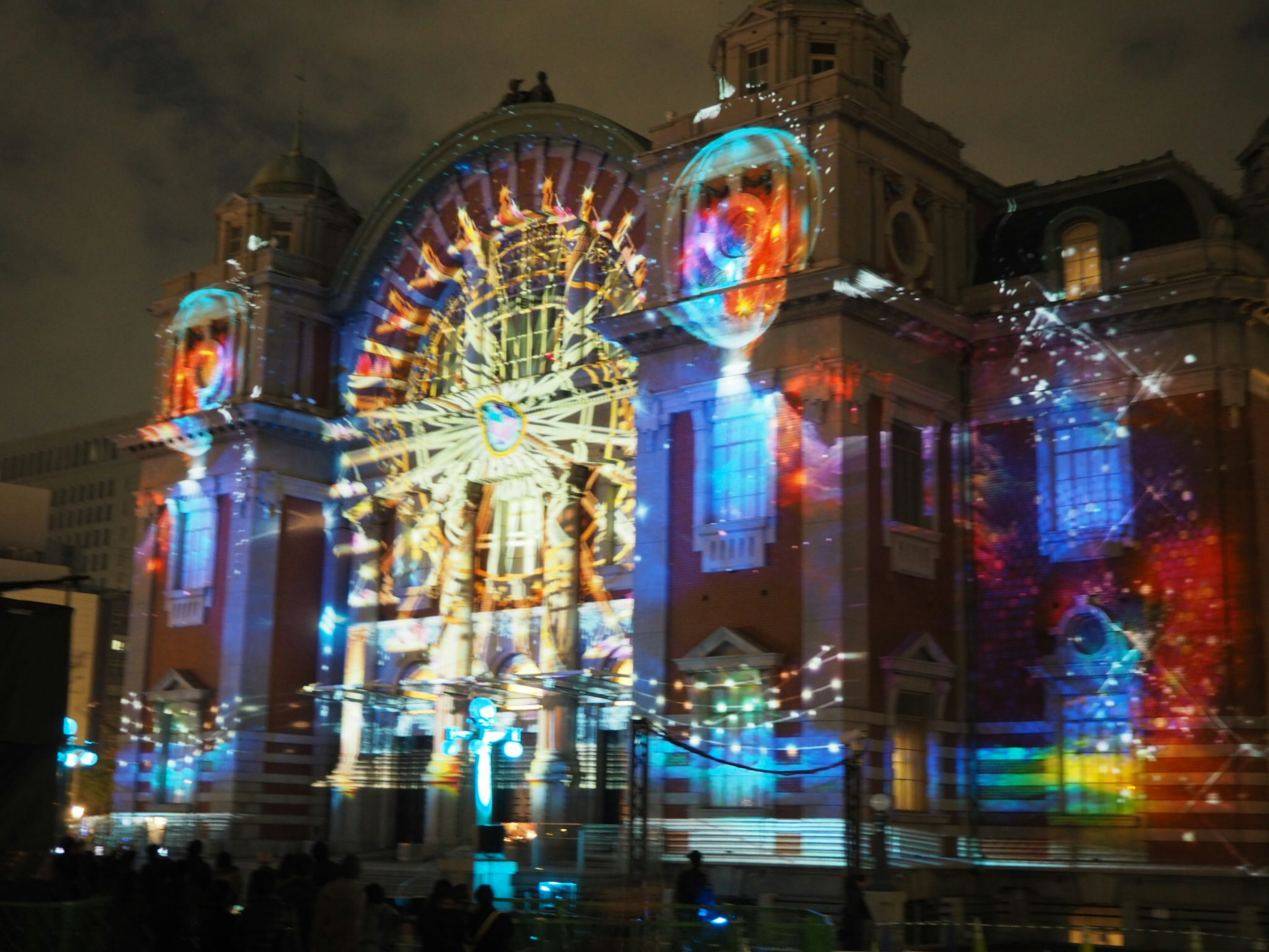 Un edificio histórico iluminado con proyecciones de luces coloridas en el cielo nocturno