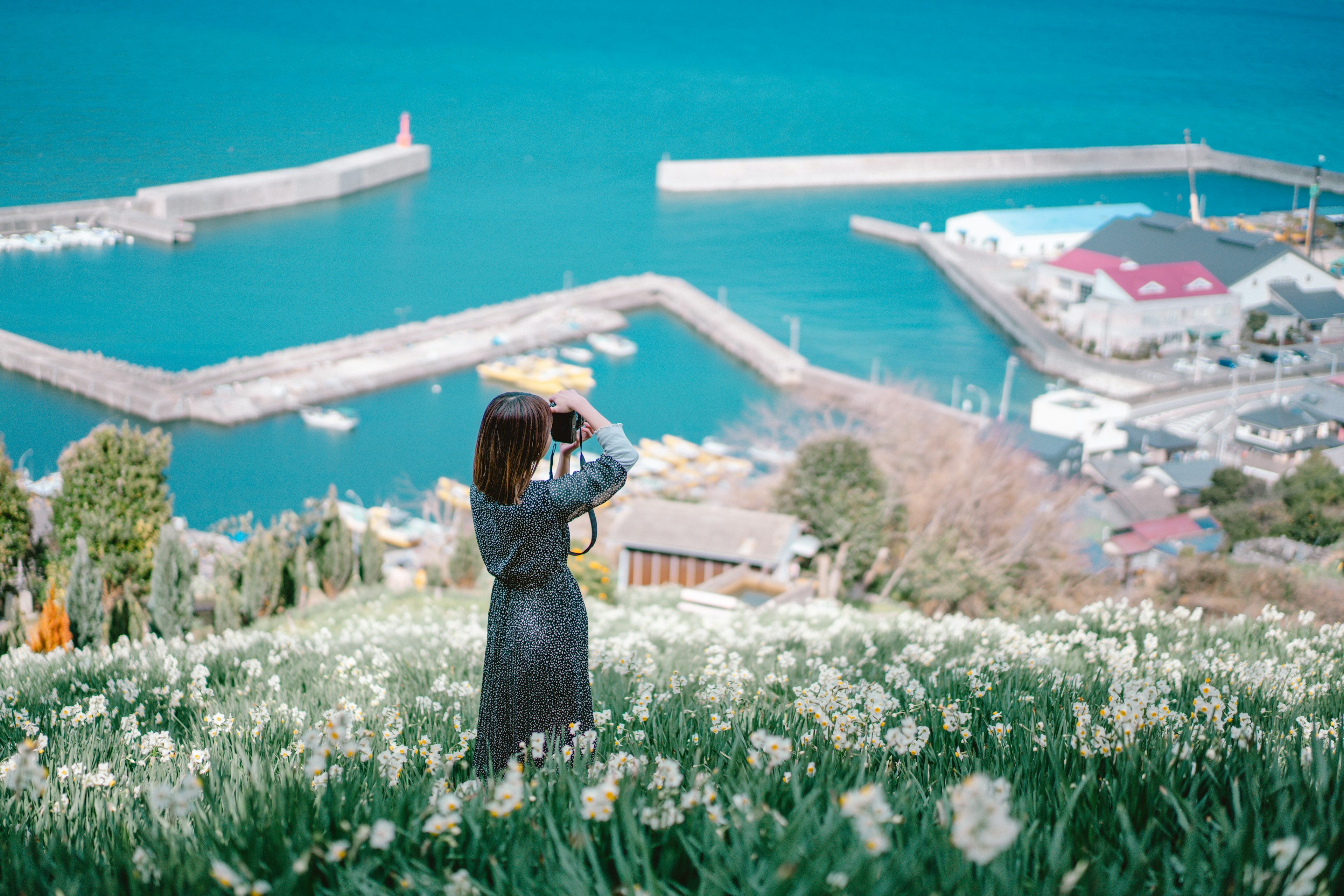 Donna con una macchina fotografica in un campo di fiori con vista sul mare blu