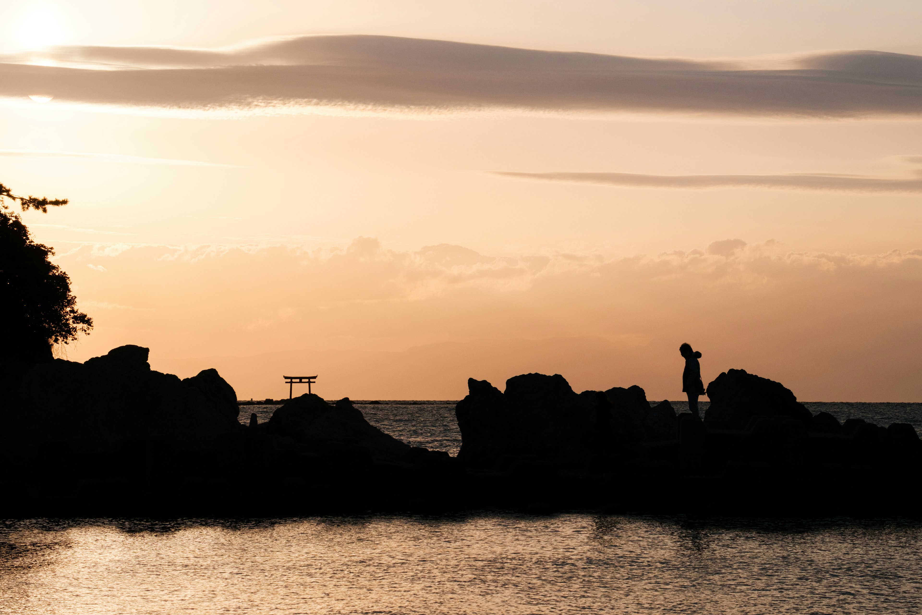 Silueta de una persona de pie sobre rocas en una playa al atardecer