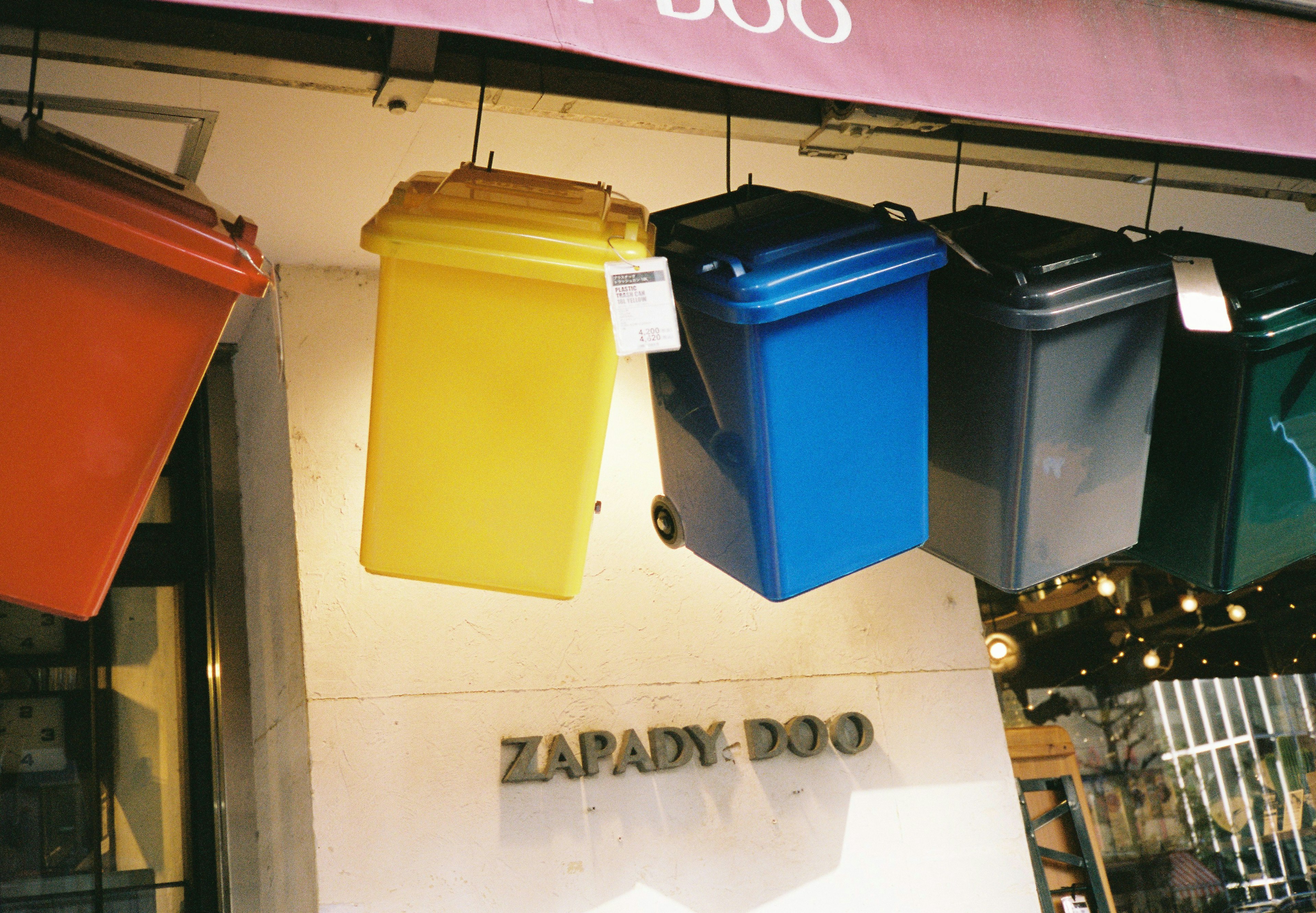 Colorful trash bins hanging outside a store with the sign Zapady-Doo