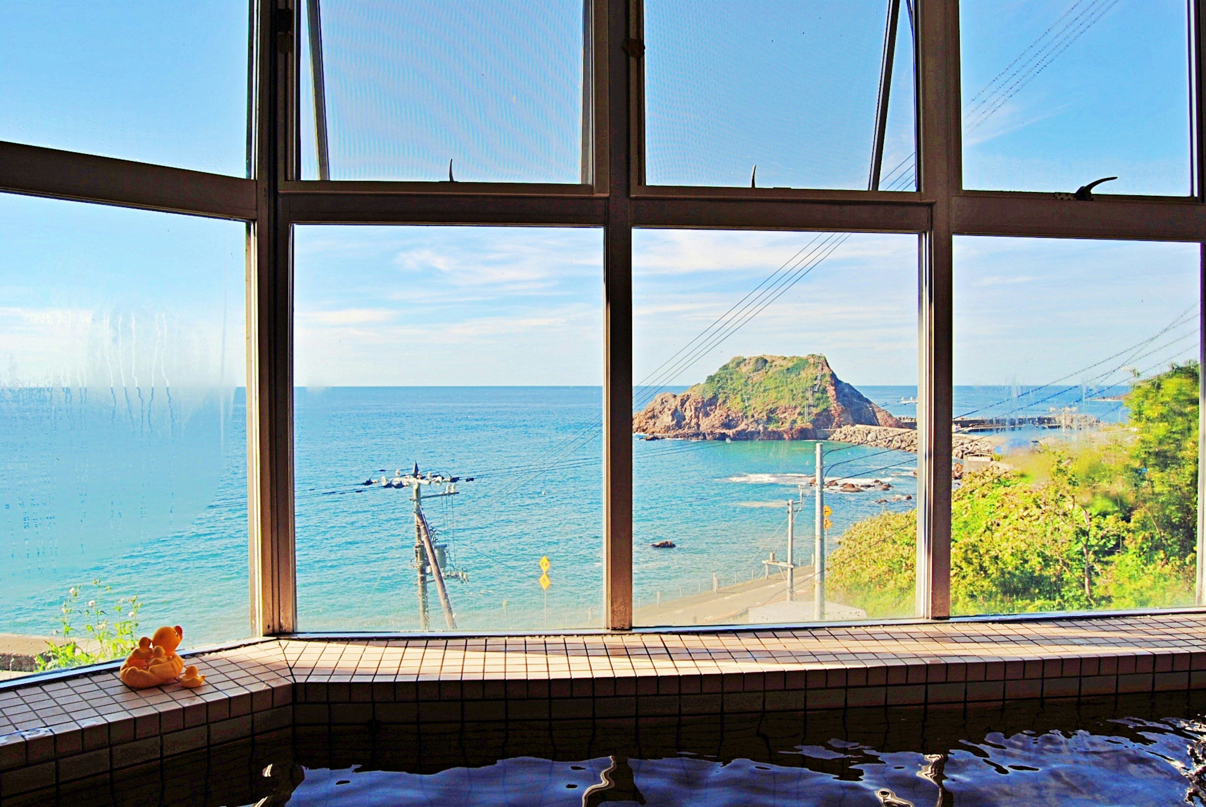 Scenic view of an onsen overlooking the sea with a small island and blue sky