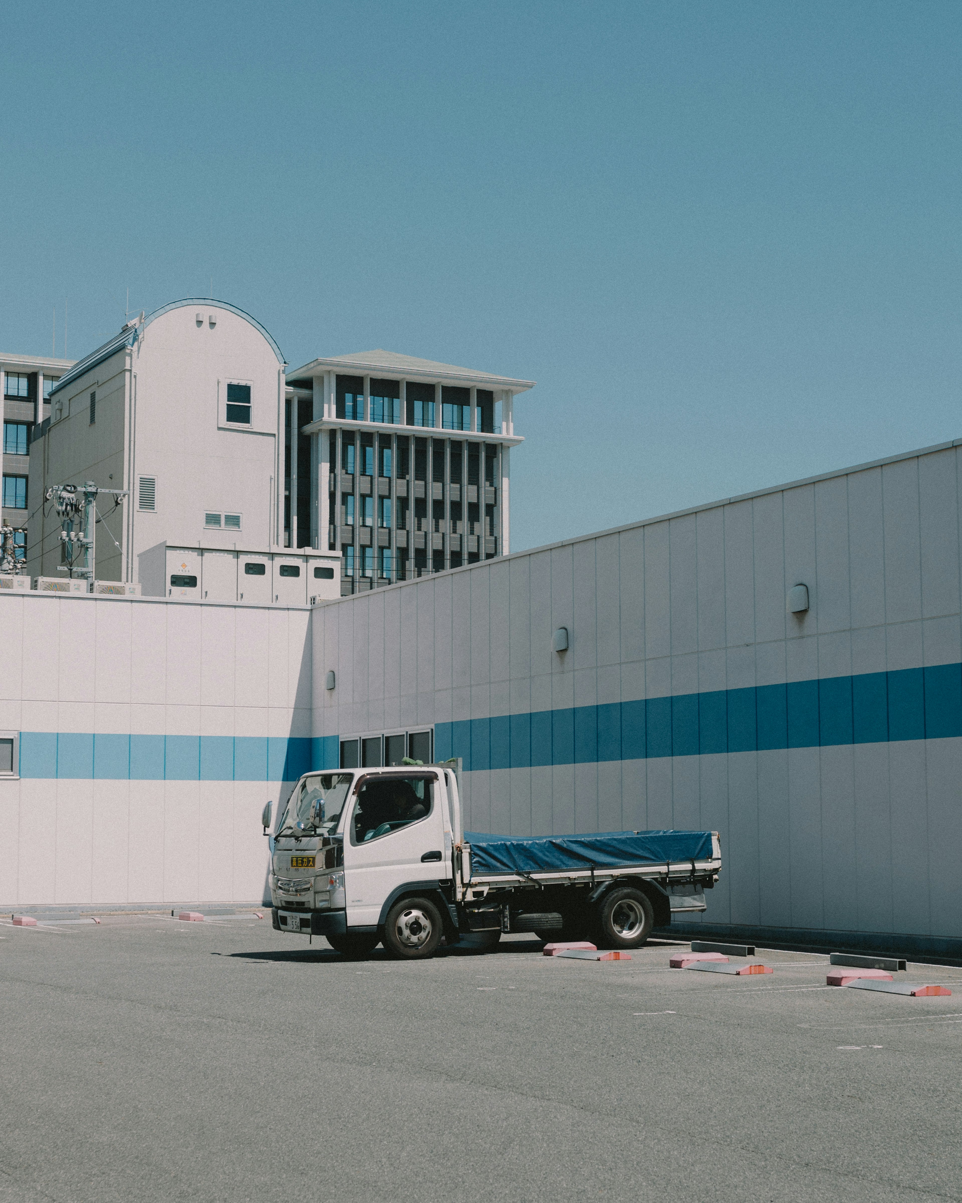 Small truck parked in front of a warehouse with a blue stripe