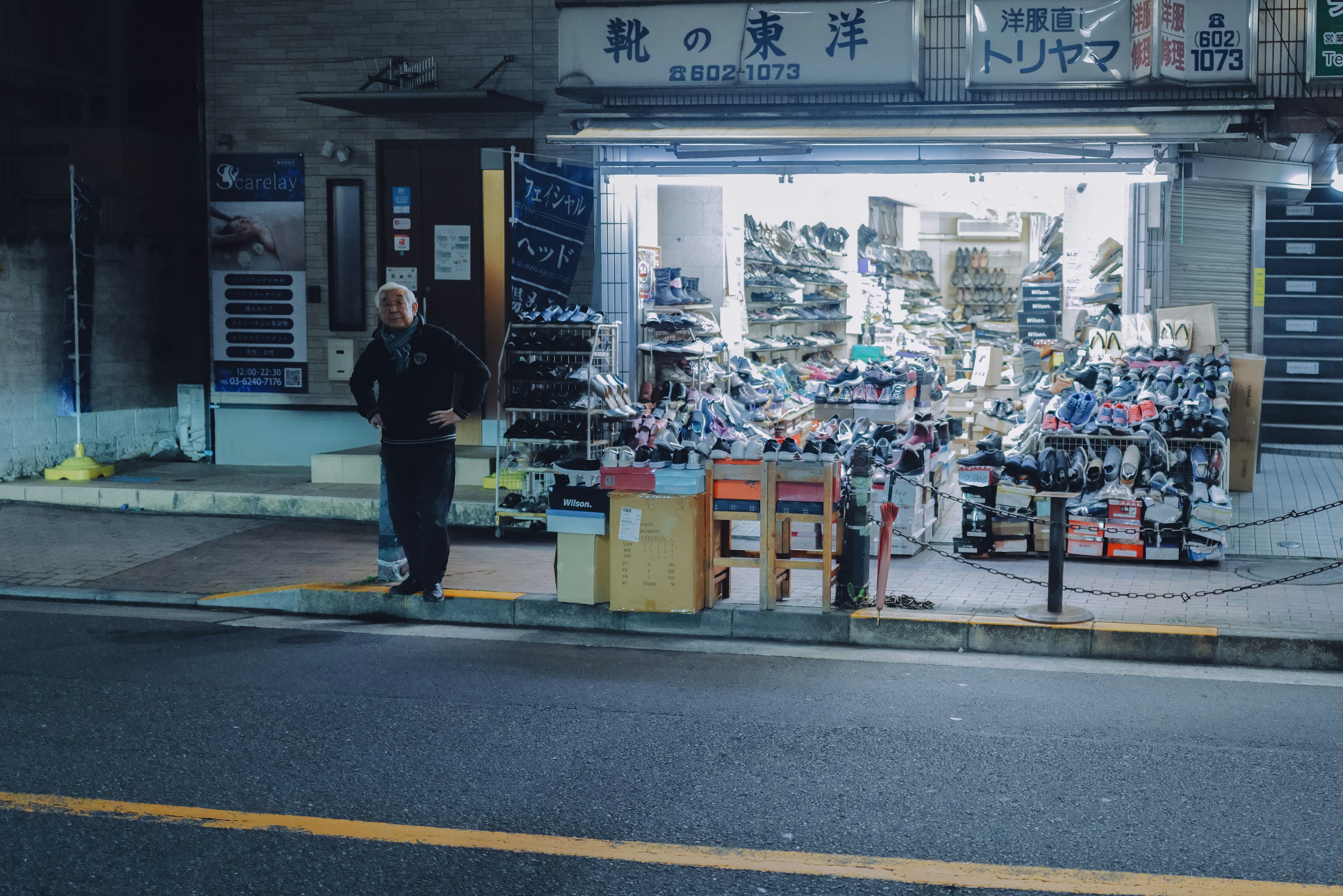 商店の外に立つ男性と靴が並ぶ光景