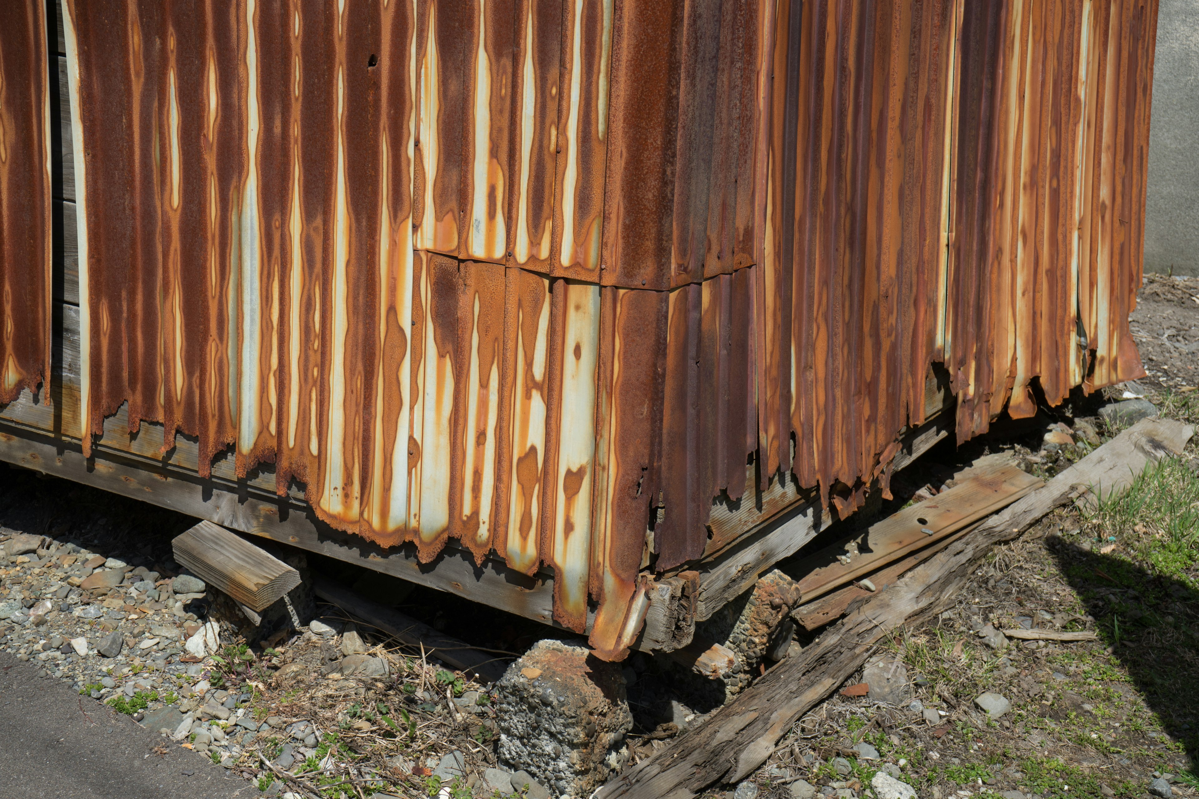 Close-up of a weathered metal shed with rust and wooden foundation