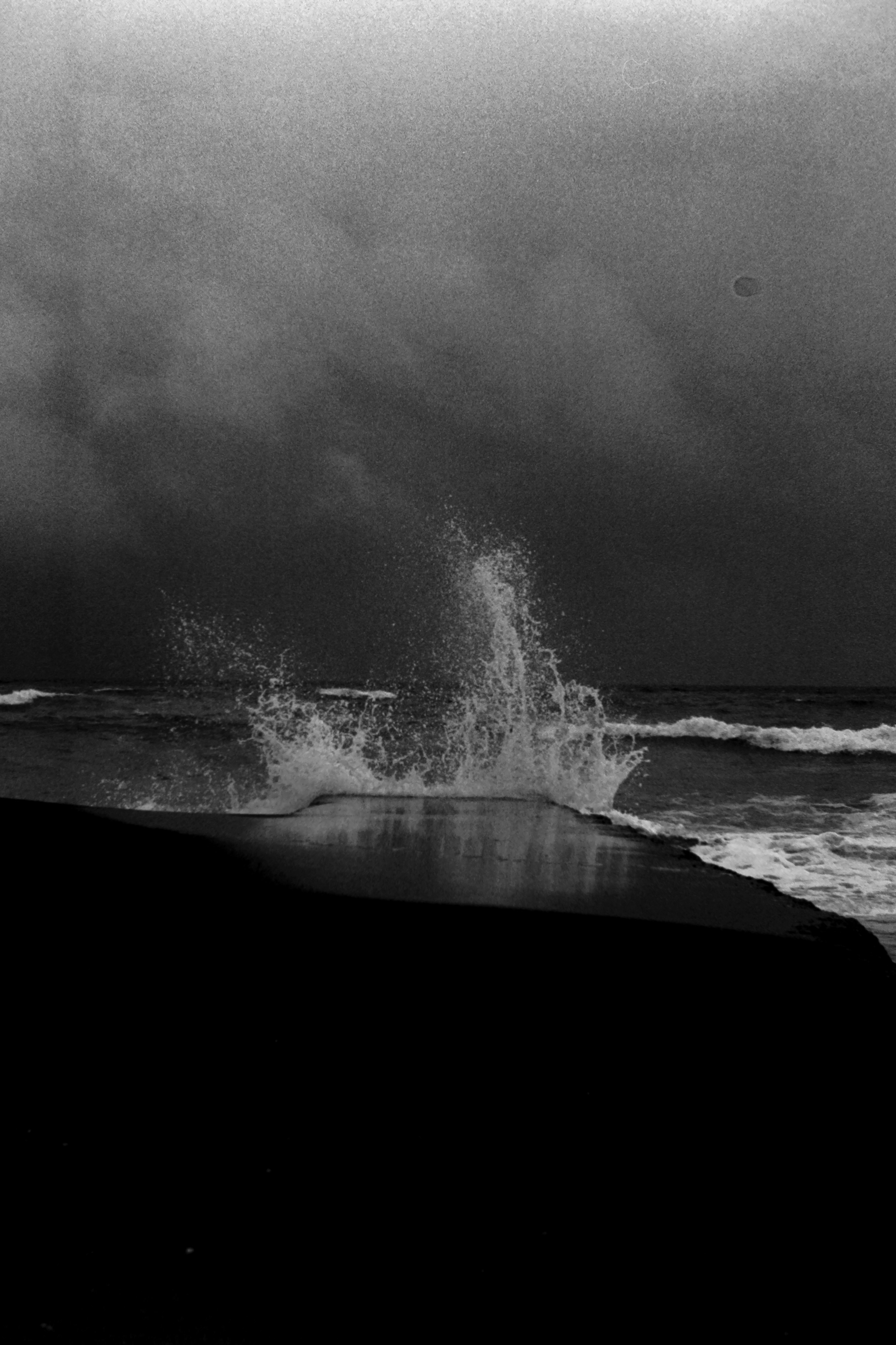 Wellen, die gegen dunkle Felsen brechen und Spritzer in einer monochromen Landschaft erzeugen