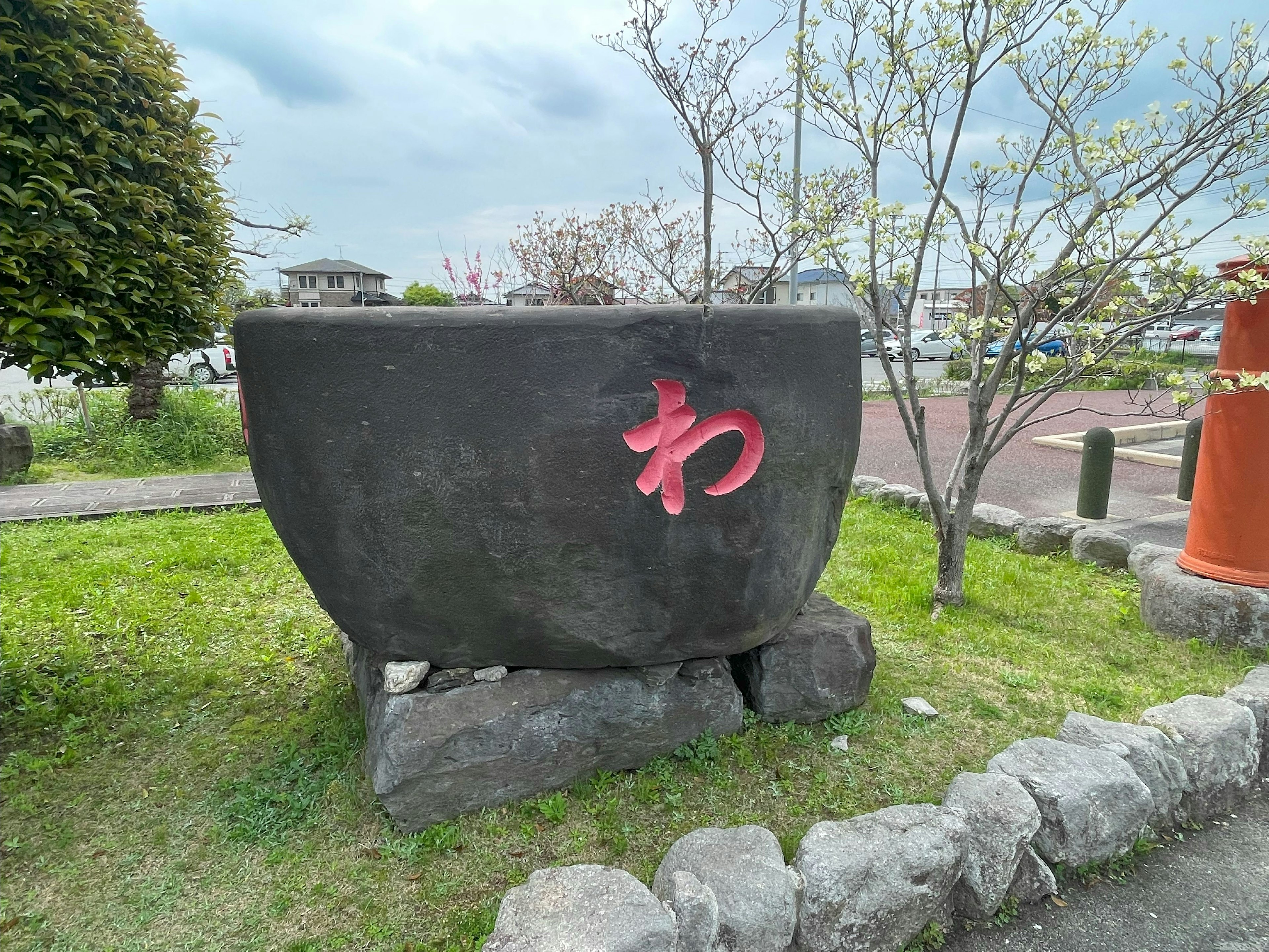 Sculpture en pierre noire avec le caractère rouge 'わ' dans un parc