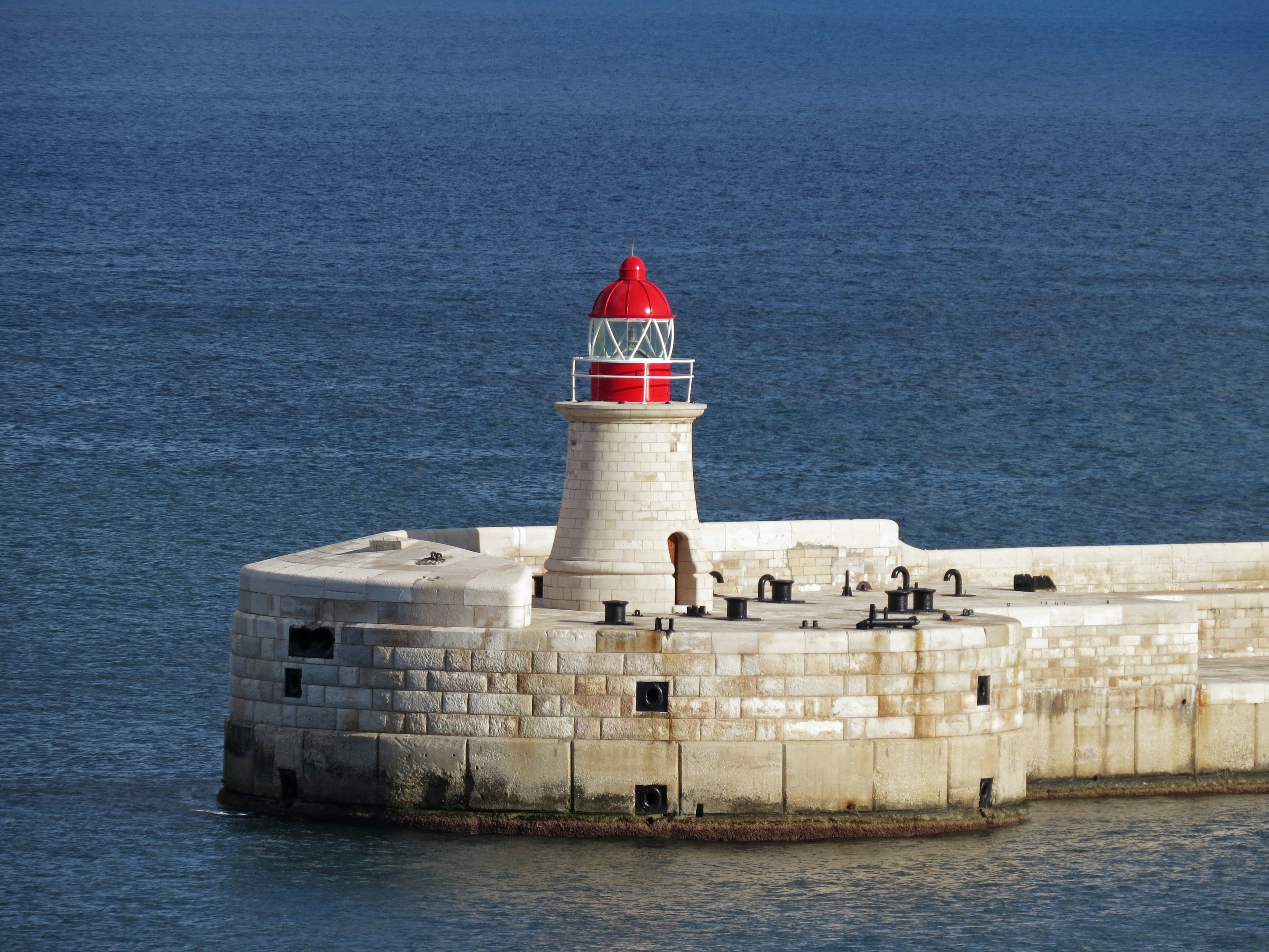 Leuchtturm mit rotem Kopf auf einem Steg am Meer