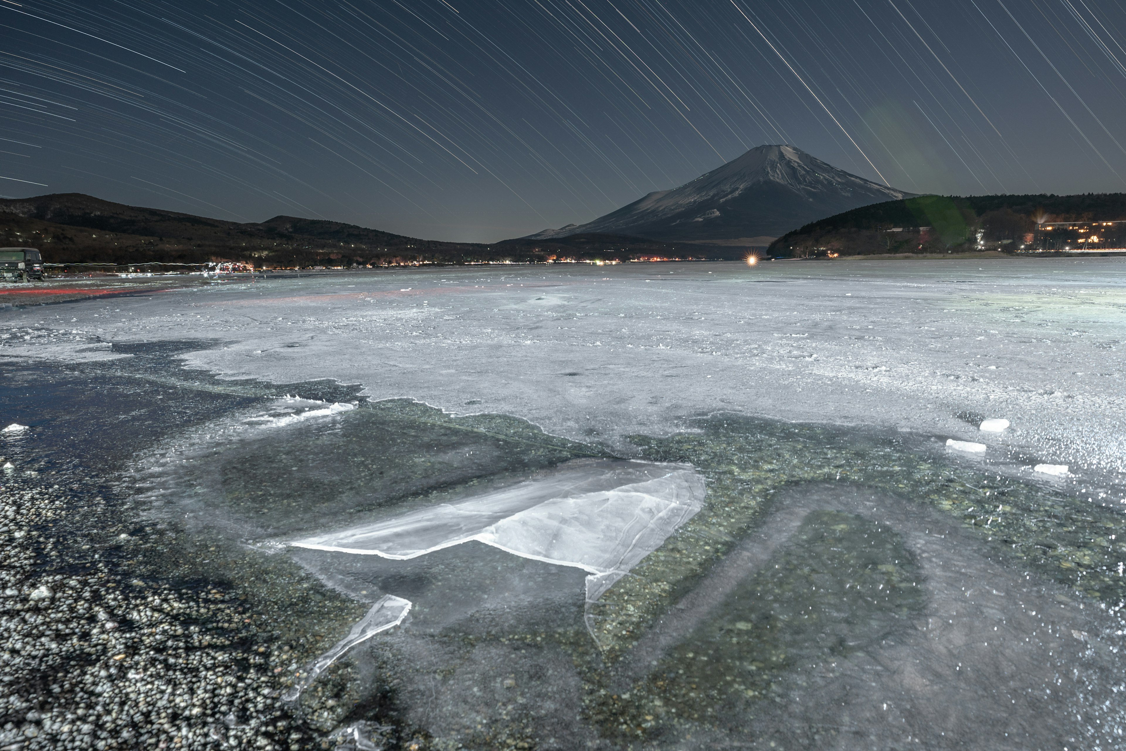 富士山と星の軌跡が見える夜の風景　凍った湖の表面に白い氷のパターン